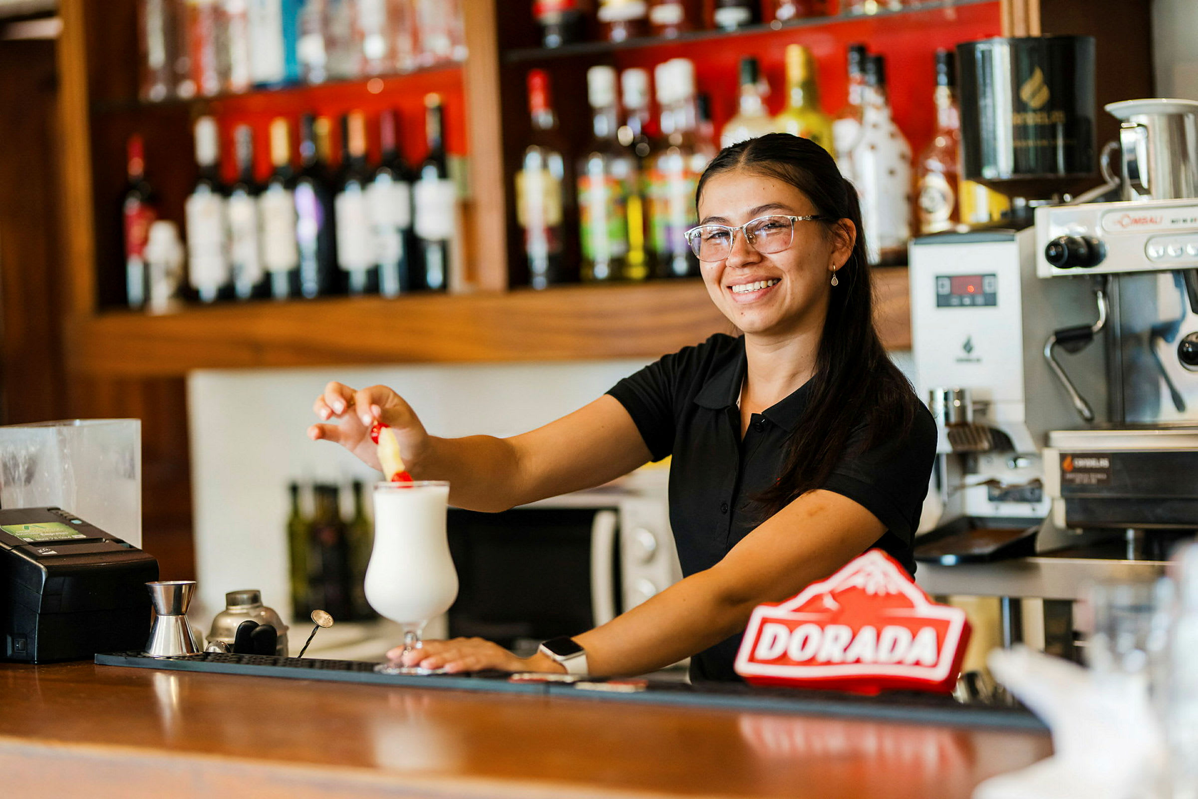 En person står ved en bardisk og dekorerer en hvid drink med en rød genstand. (AI-genereret tekst)