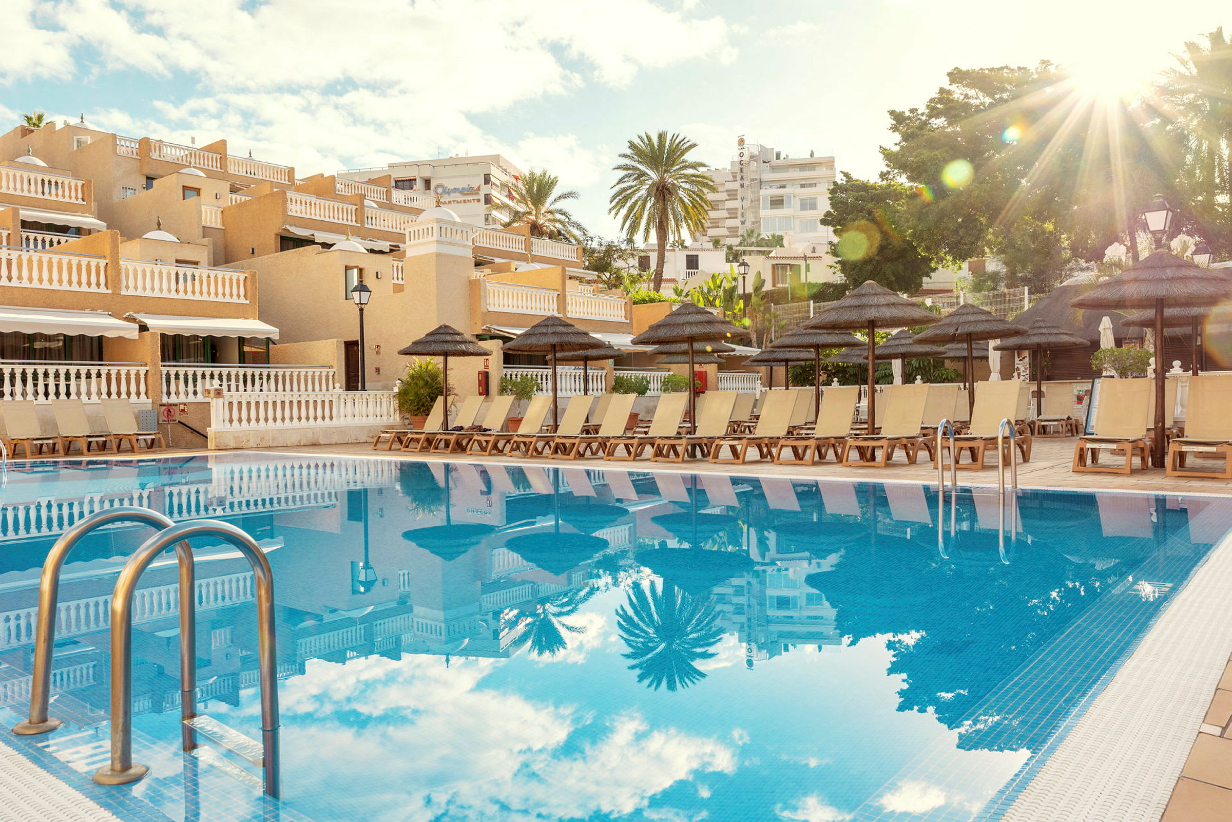 En udendørs swimmingpool med liggestole og parasoller ved et hotel. (AI-genereret tekst)