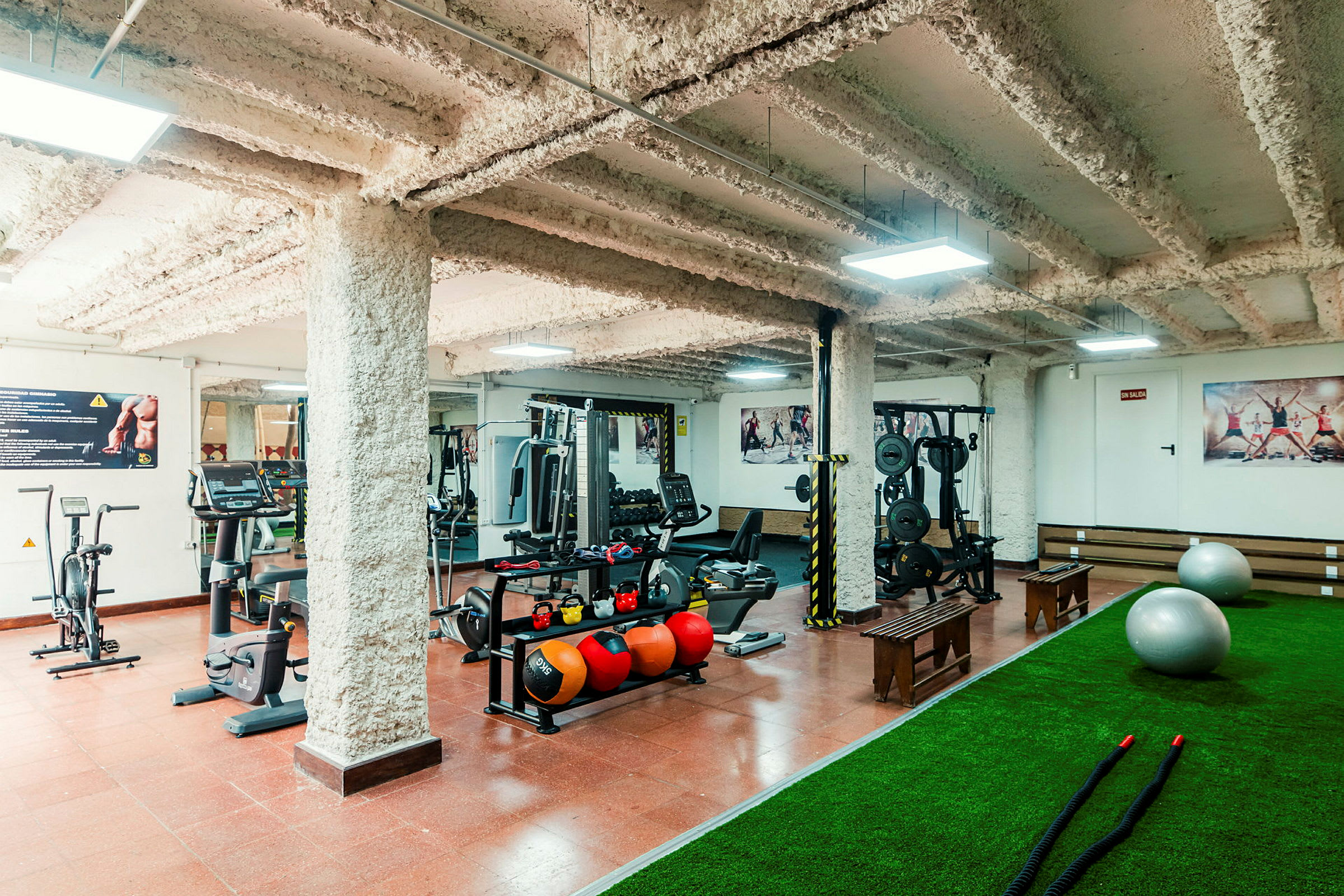 Et fitnesscenter med træningsmaskiner, vægte, medicinbolde, måtter og pilatesbolde. (AI-genereret tekst)