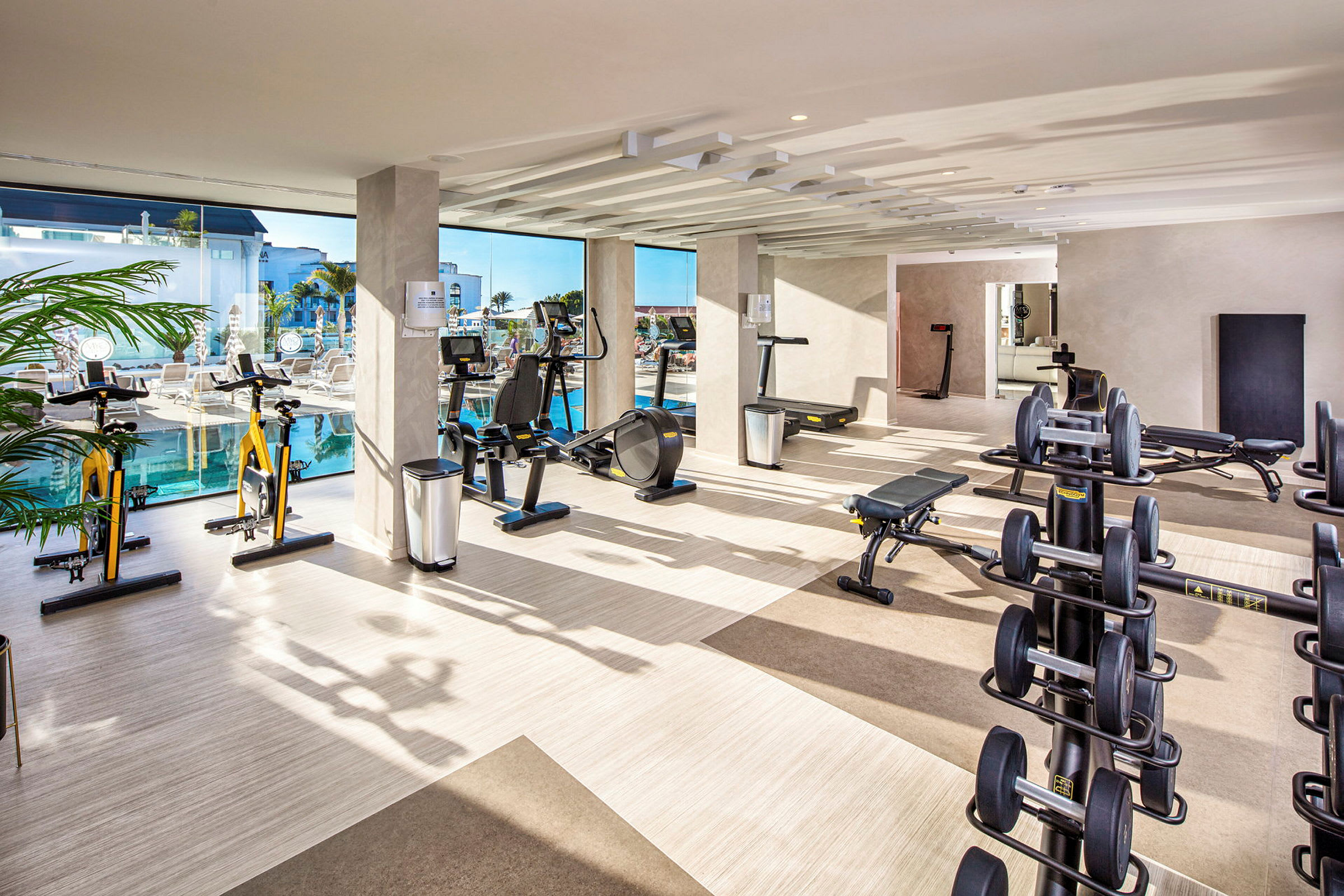 Et fitnesscenter med træningsudstyr og store vinduer, der vender ud mod en pool. (AI-genereret tekst)