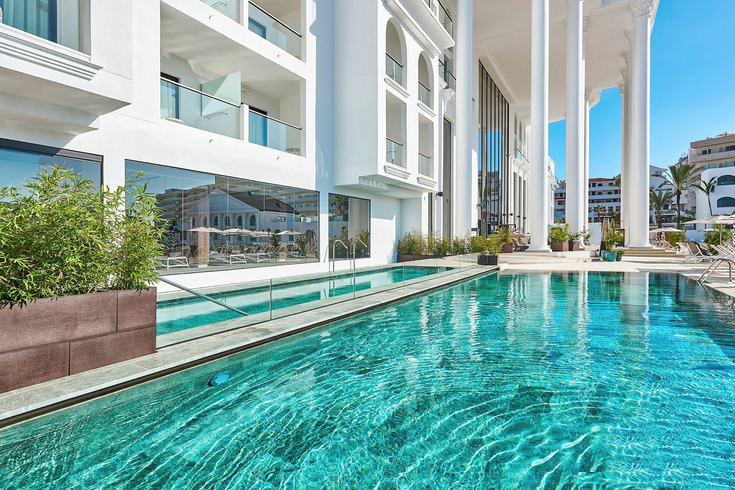En udendørs pool ved et hvidt hotel med glasfacade og store søjler. (AI-genereret tekst)