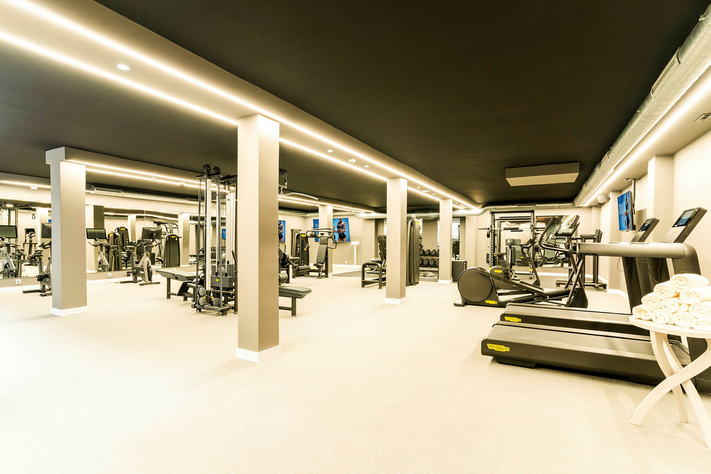 Et moderne fitnesscenter med forskellige træningsmaskiner og udstyr samt løbebånd og håndklæder ved siden af. (AI-genereret tekst)