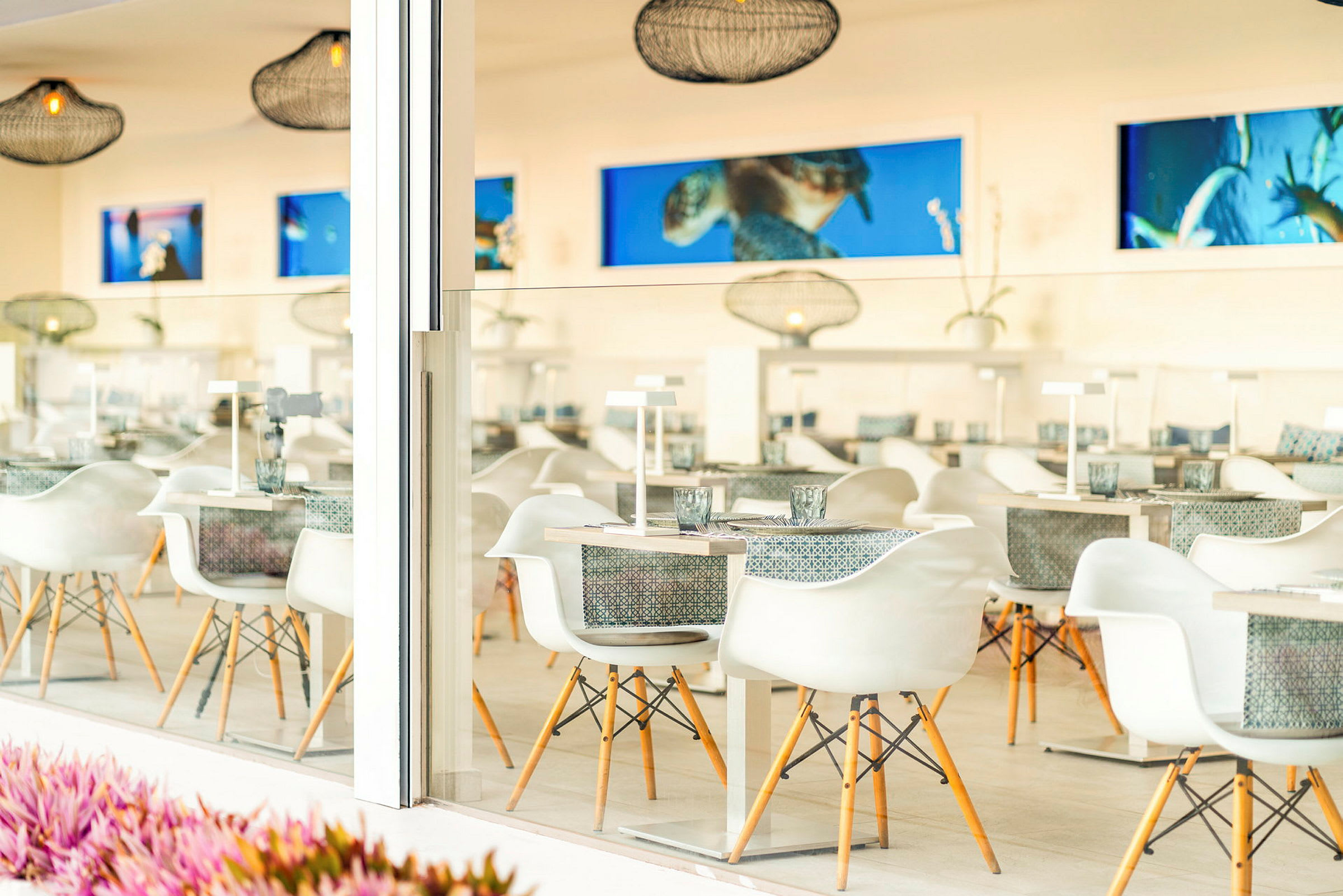 En moderne og lys restaurant med hvide stole og dækkede borde, dekoreret med hængende lamper og kunstværker på væggene. (AI-genereret tekst)