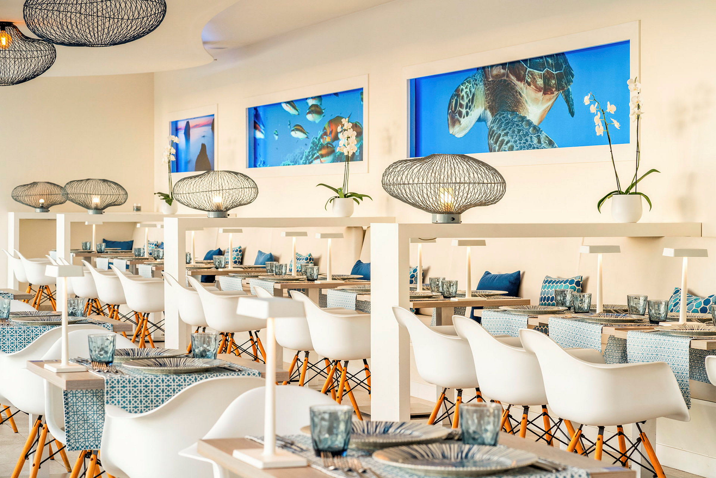 Indretning af en lys og moderne restaurant med stilfulde borde, hvide stole, dekorative lamper og maritime detaljer. (AI-genereret tekst)