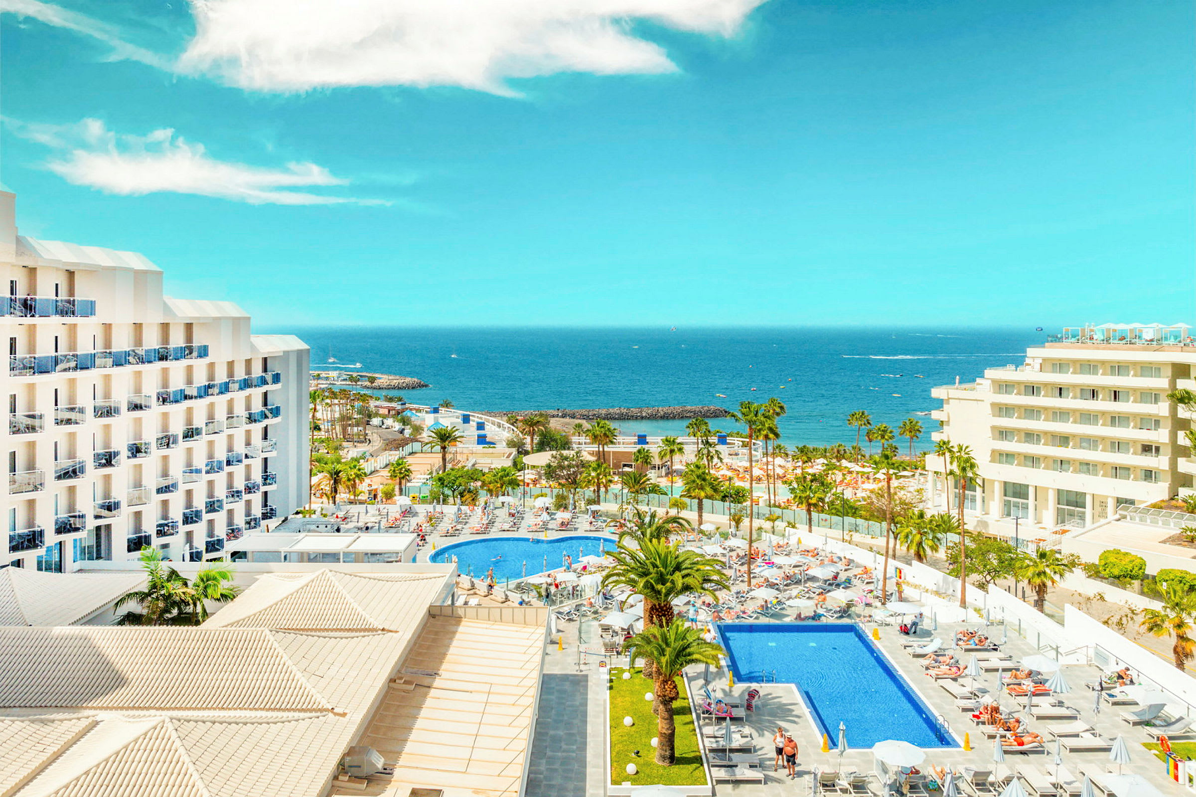 Hotel med poolområde og palmer ved kysten med havudsigt. (AI-genereret tekst)