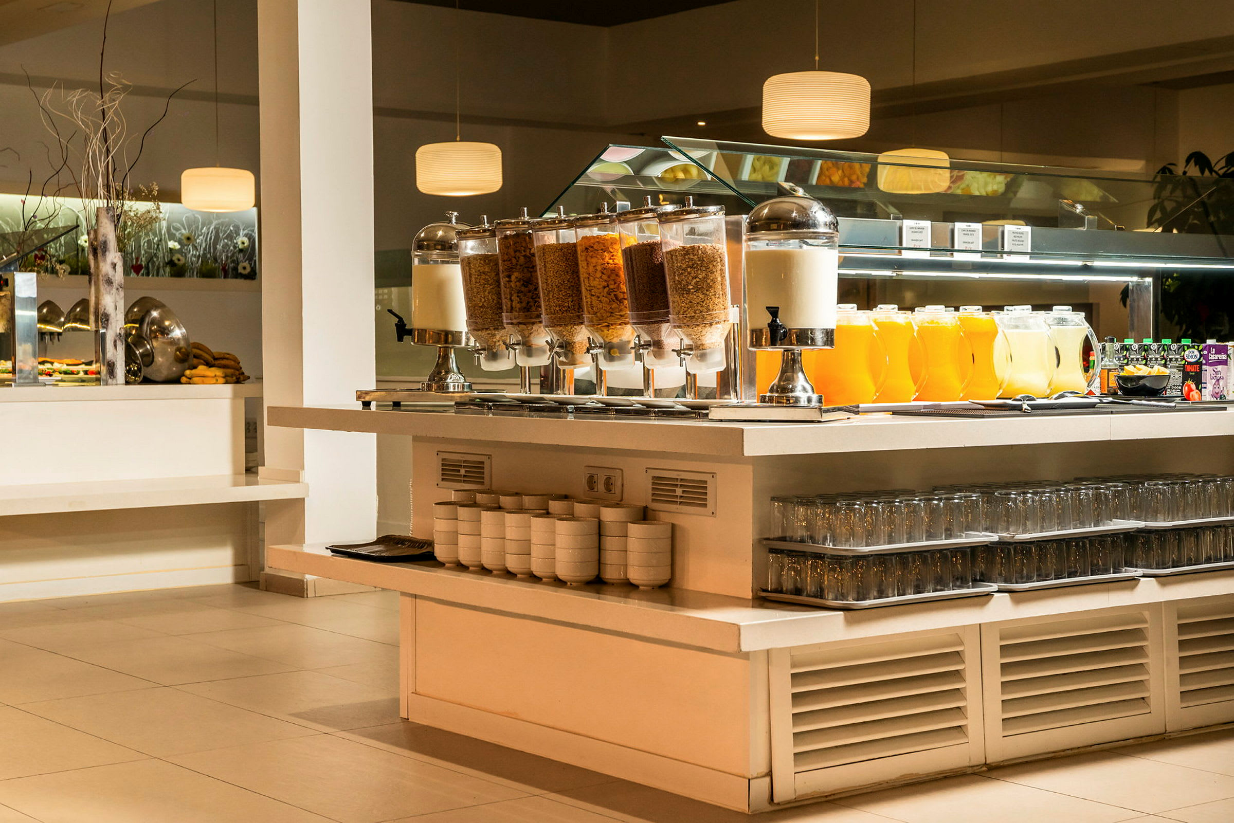 Buffetbord med forskellige morgenmadsvalg, inklusive kornbeholdere, mælkedispenser, juicekolber og glas. (AI-genereret tekst)