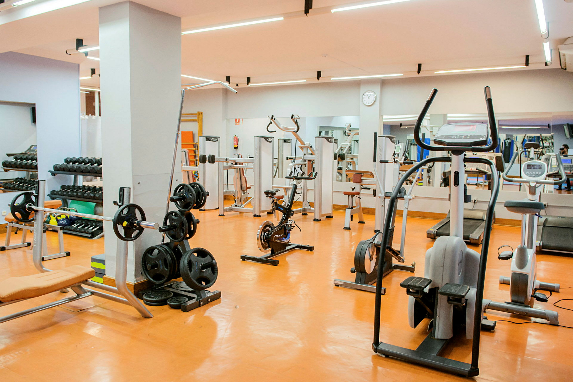 Et fuldt udstyret fitnesscenter med træningsudstyr og maskiner. Spejle kan ses i baggrunden. (AI-genereret tekst)