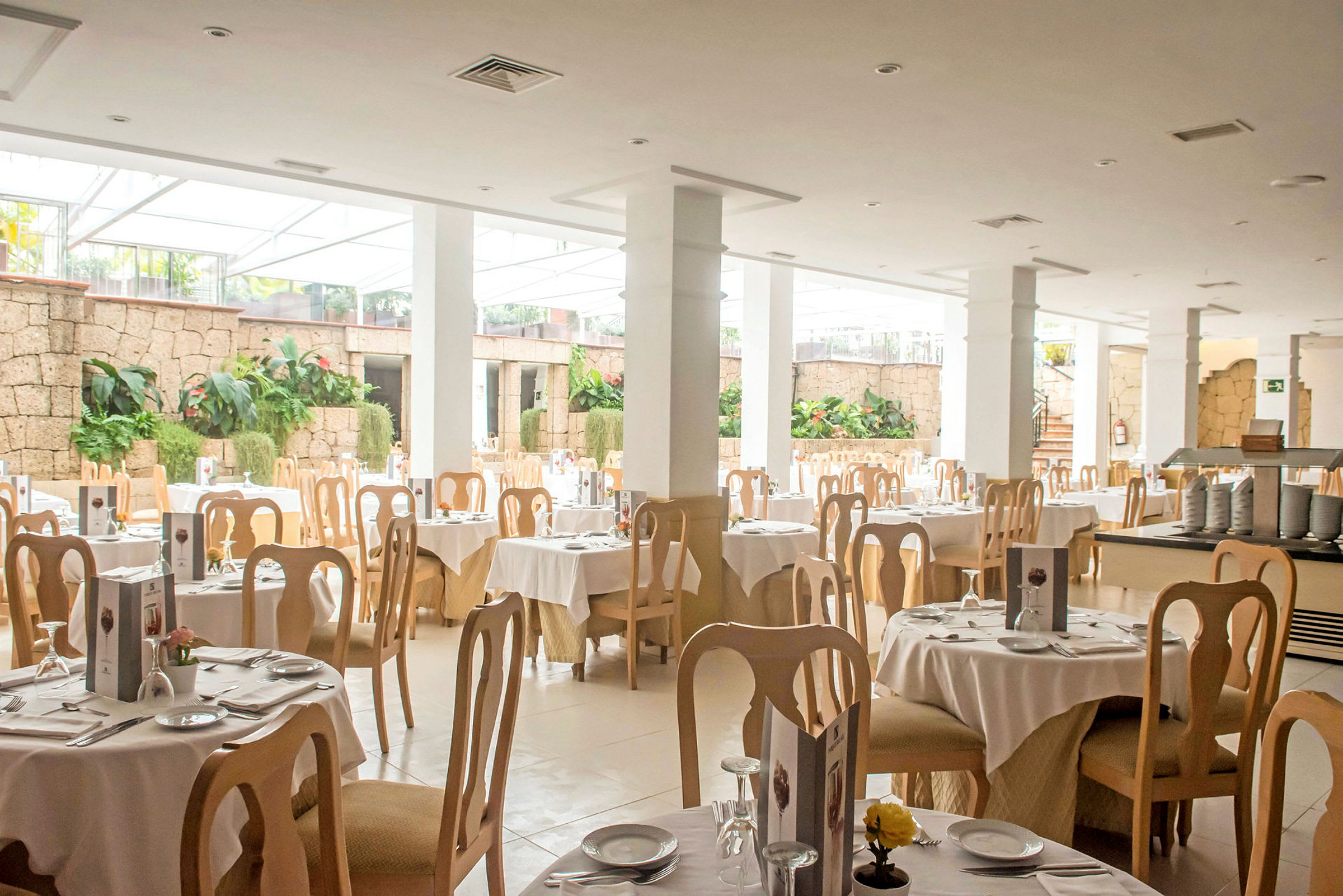 Lys restaurant med dækkede borde og træstole. (AI-genereret tekst)