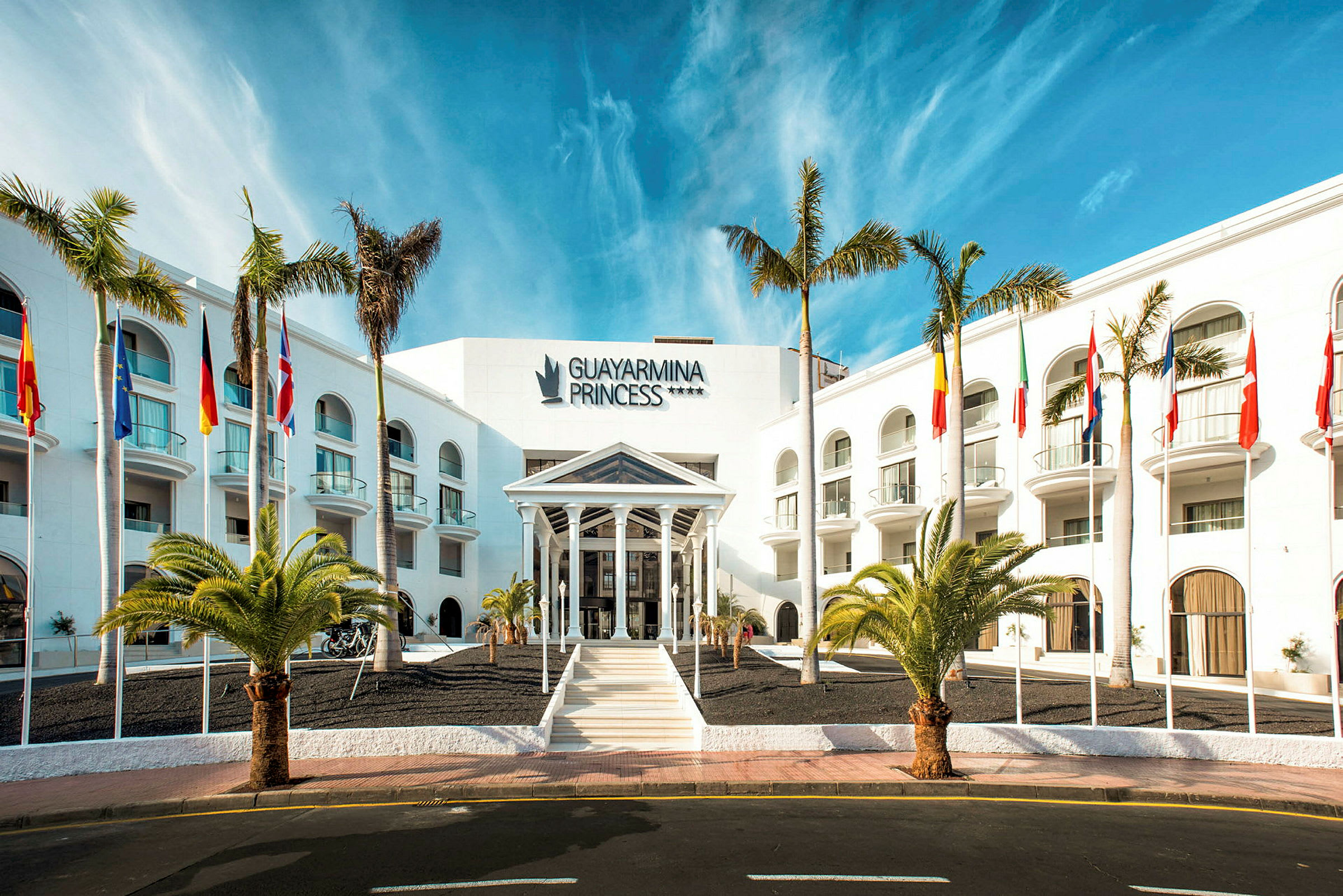 Hotel Guayarmina Princess med palmer og flag ved indgangen. (AI-genereret tekst)