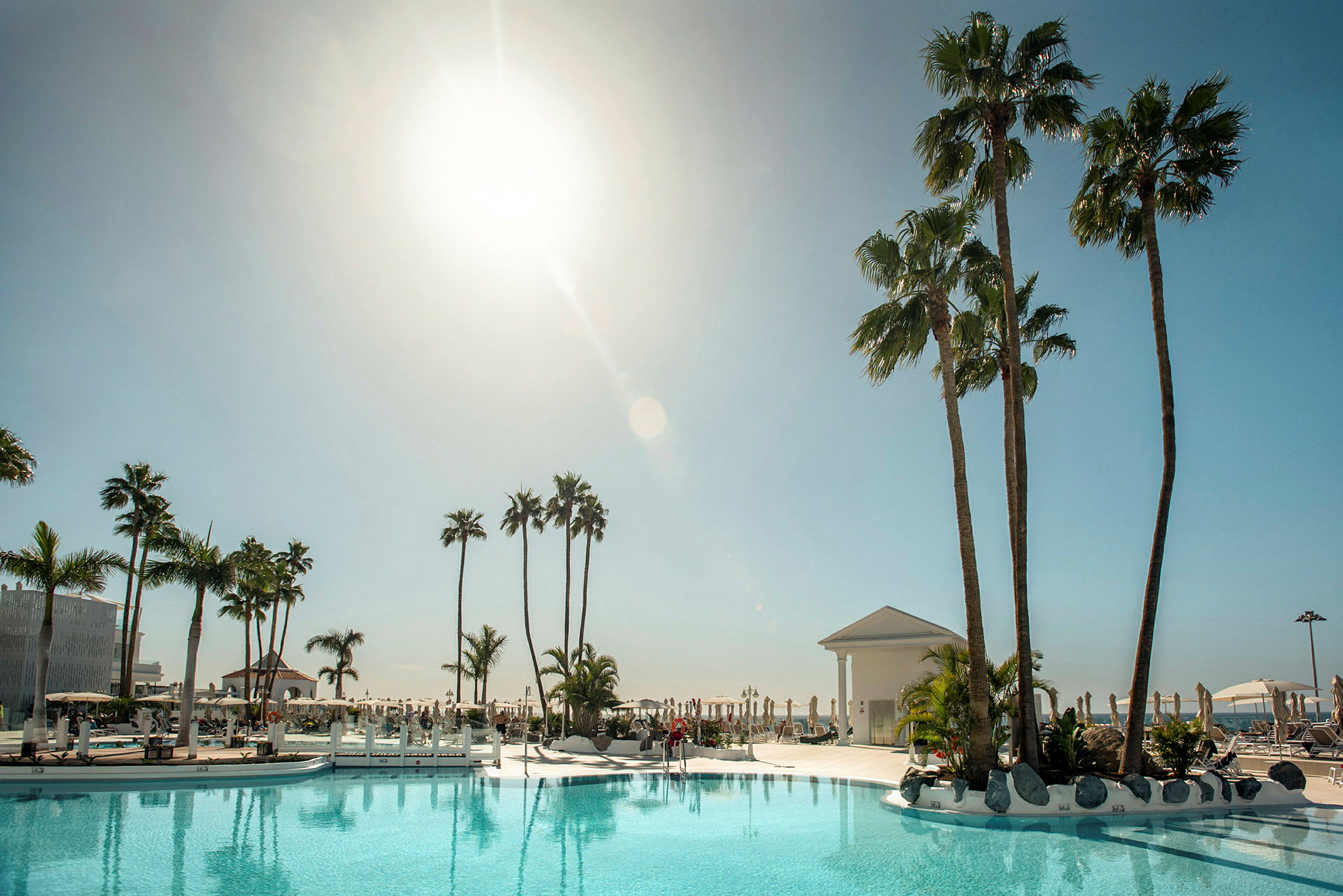 Udendørs swimmingpool med liggestole og palmer omgivet af en klar himmel. (AI-genereret tekst)