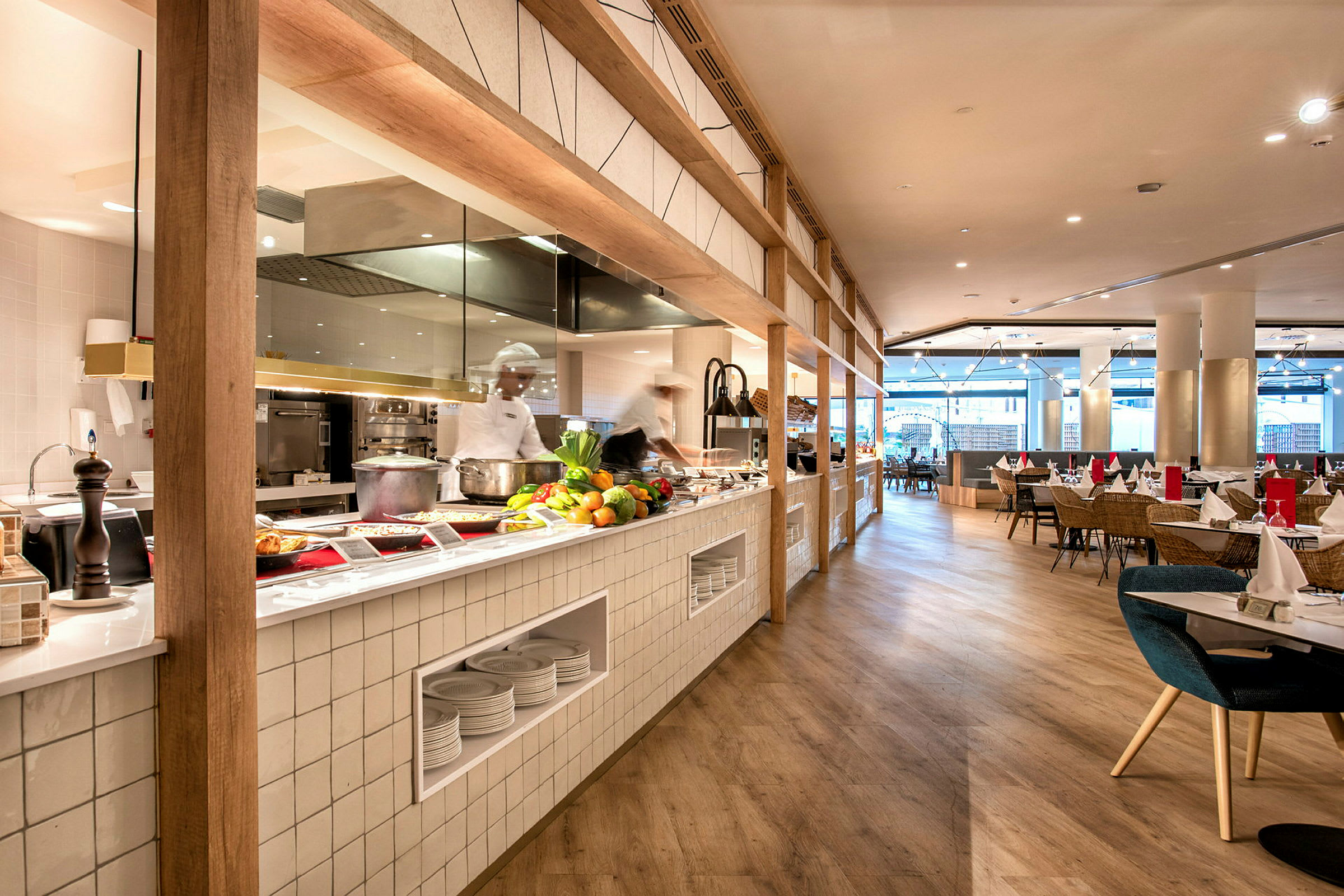 Billede af en moderne restaurant med åbent køkken, bænk med friske råvarer og madservering samt siddepladser bagved. (AI-genereret tekst)