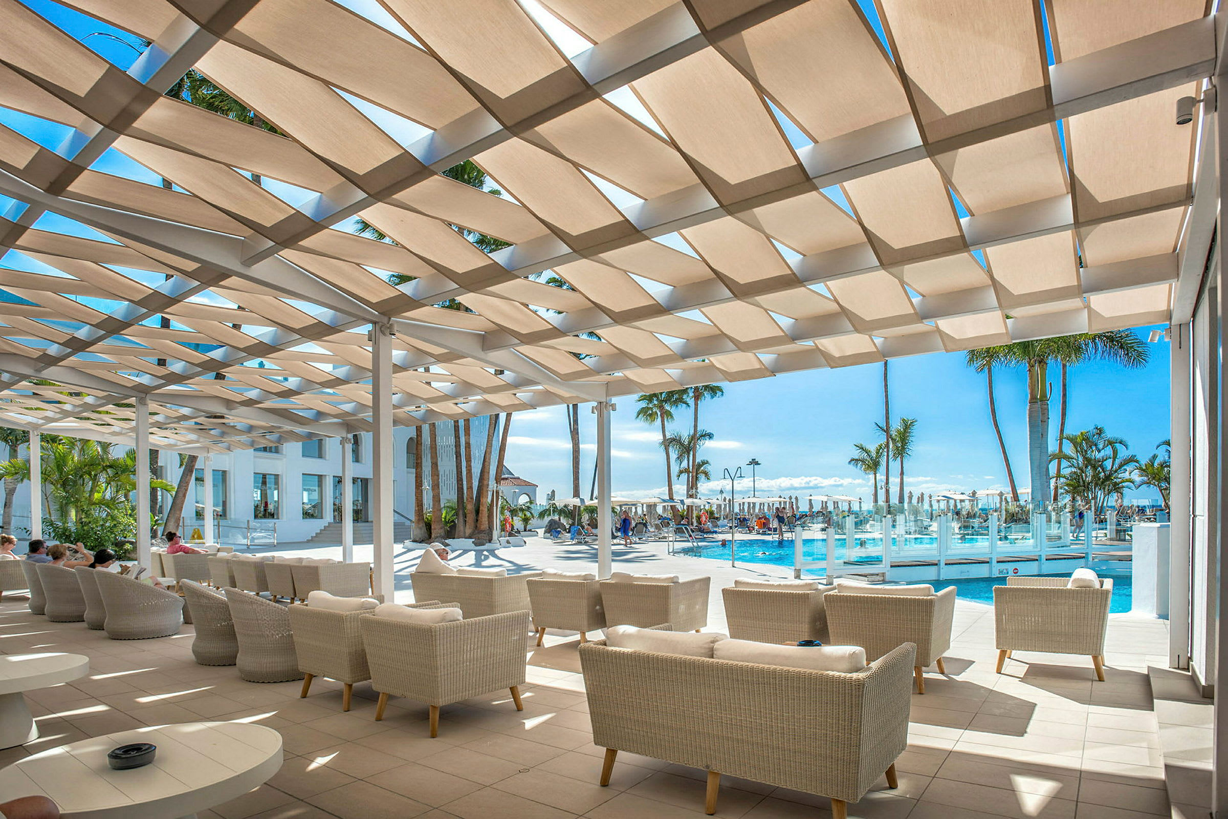 Loungeområde med sofaer under en skyggefuld pergola ved en pool. (AI-genereret tekst)