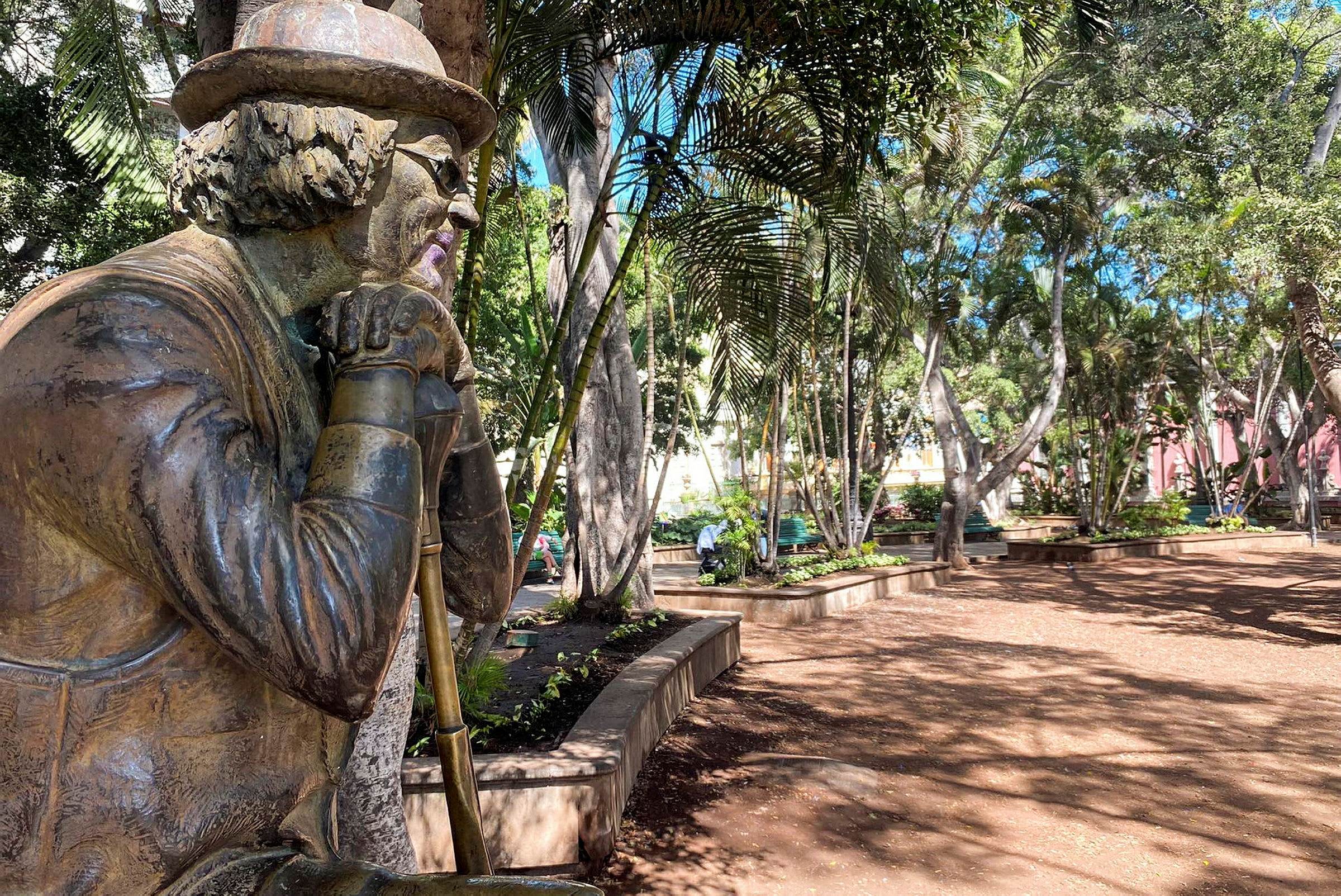 En statue af en person med hat og briller, placeret i en frodig park. (AI-genereret tekst)