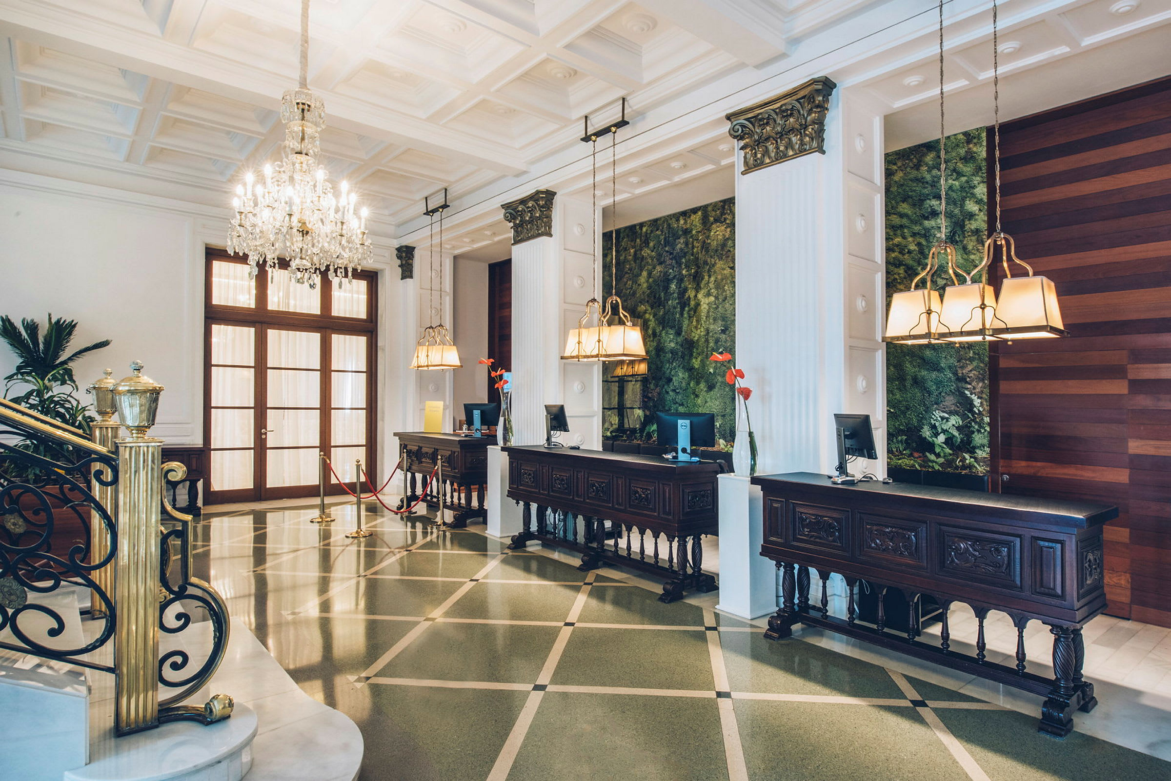 Hotellets reception med elegante møbler, lysekroner og et grønt dekoreret område i baggrunden. (AI-genereret tekst)