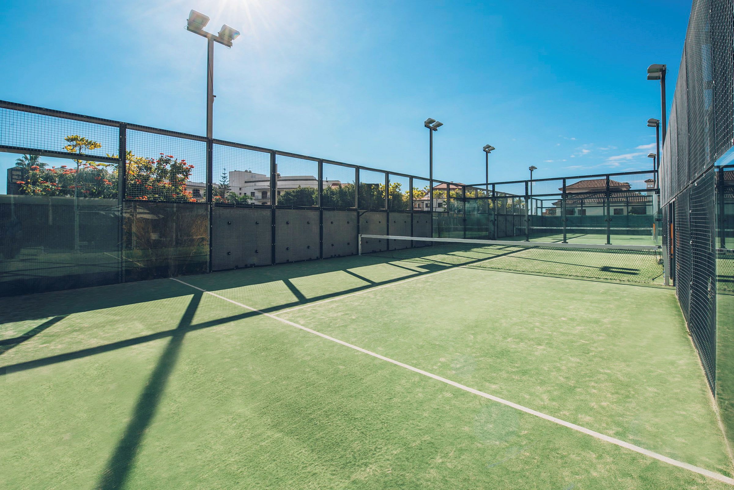 En udendørs padelbane med grøn overflade og omgivet af glas og netværk. (AI-genereret tekst)