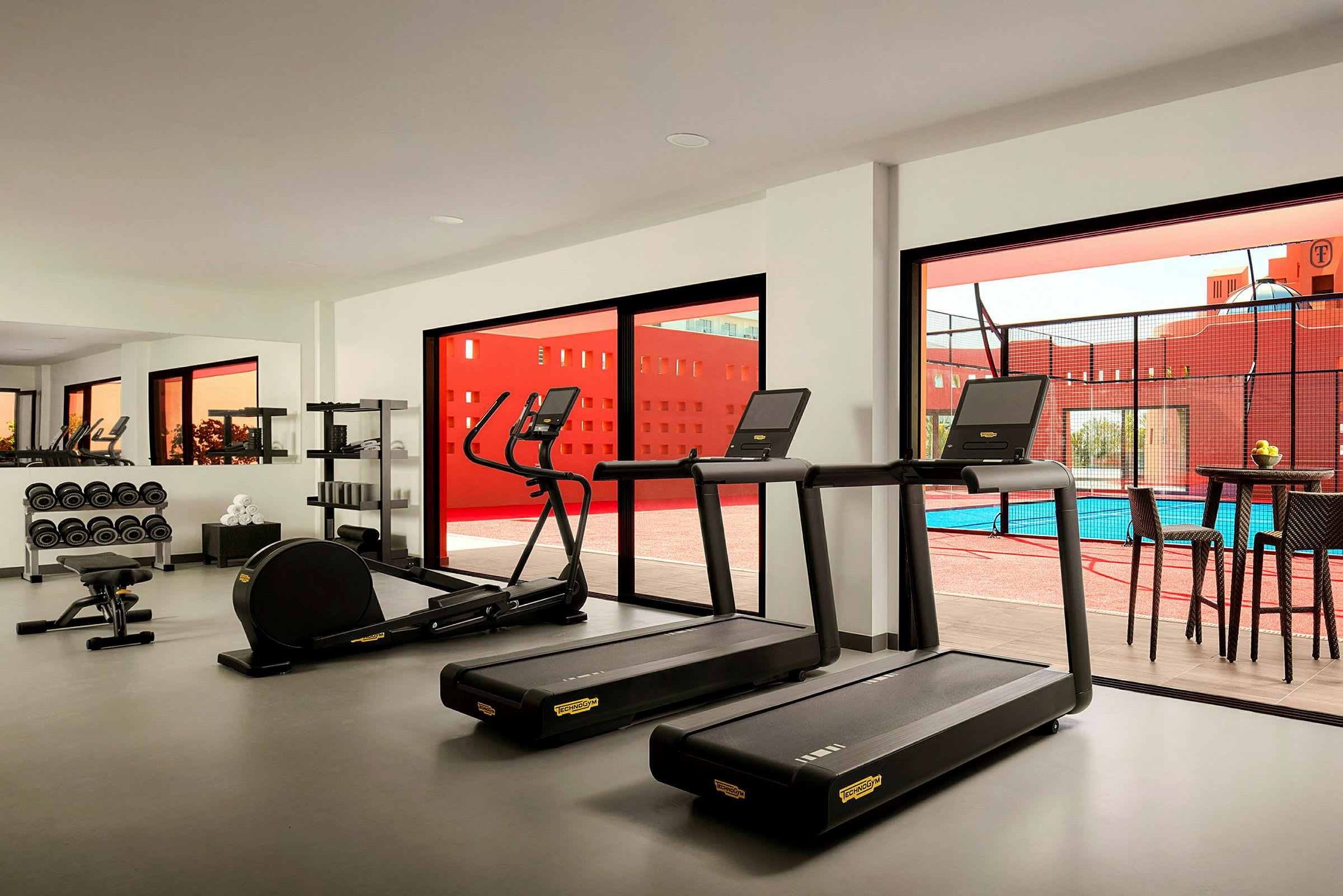 Fitnessrum med træningsmaskiner og vægte, vinduer med udsigt til en pool. (AI-genereret tekst)