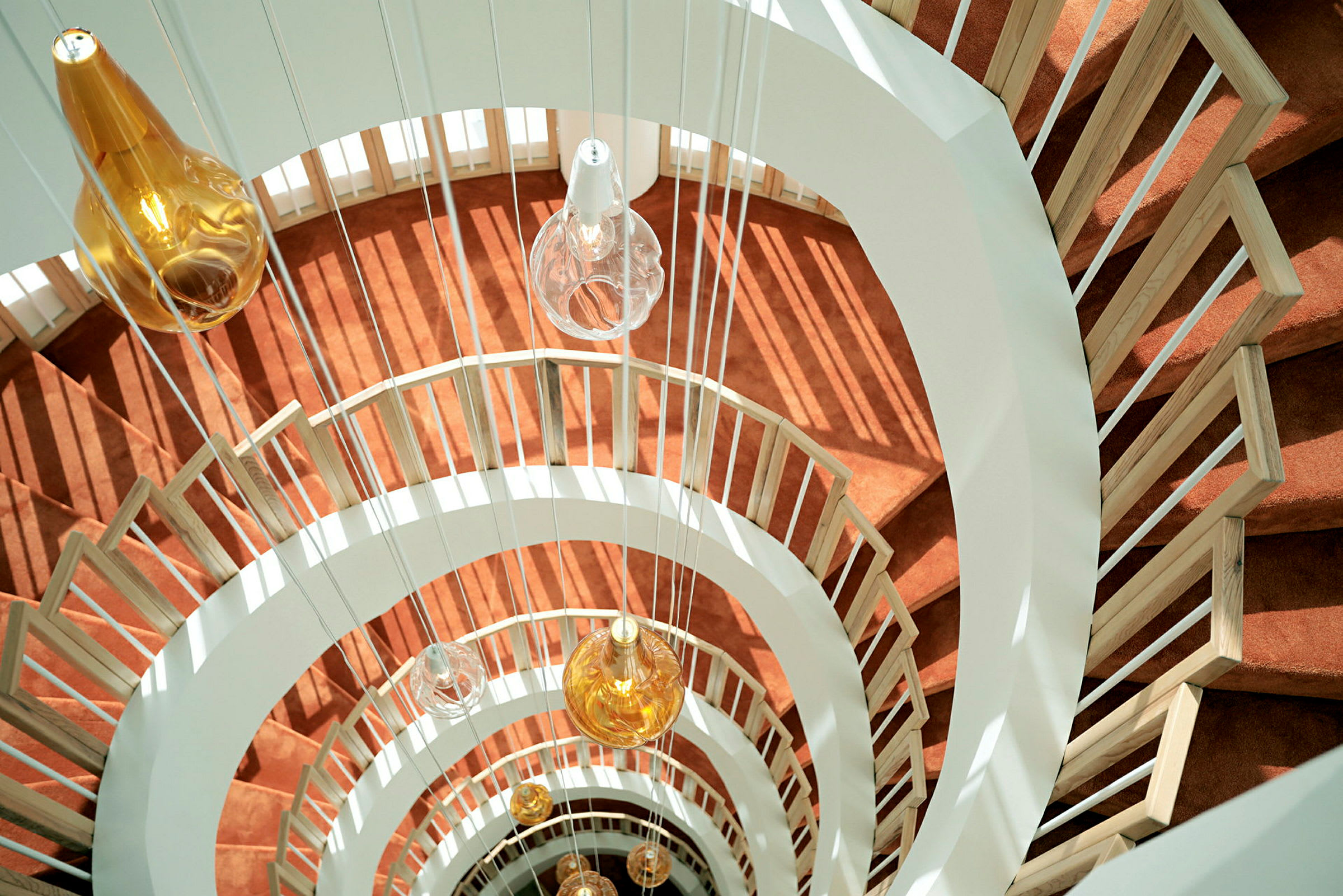 En spiraltrappe med orange tæppe og hængende lamper med glasskærme. (AI-genereret tekst)