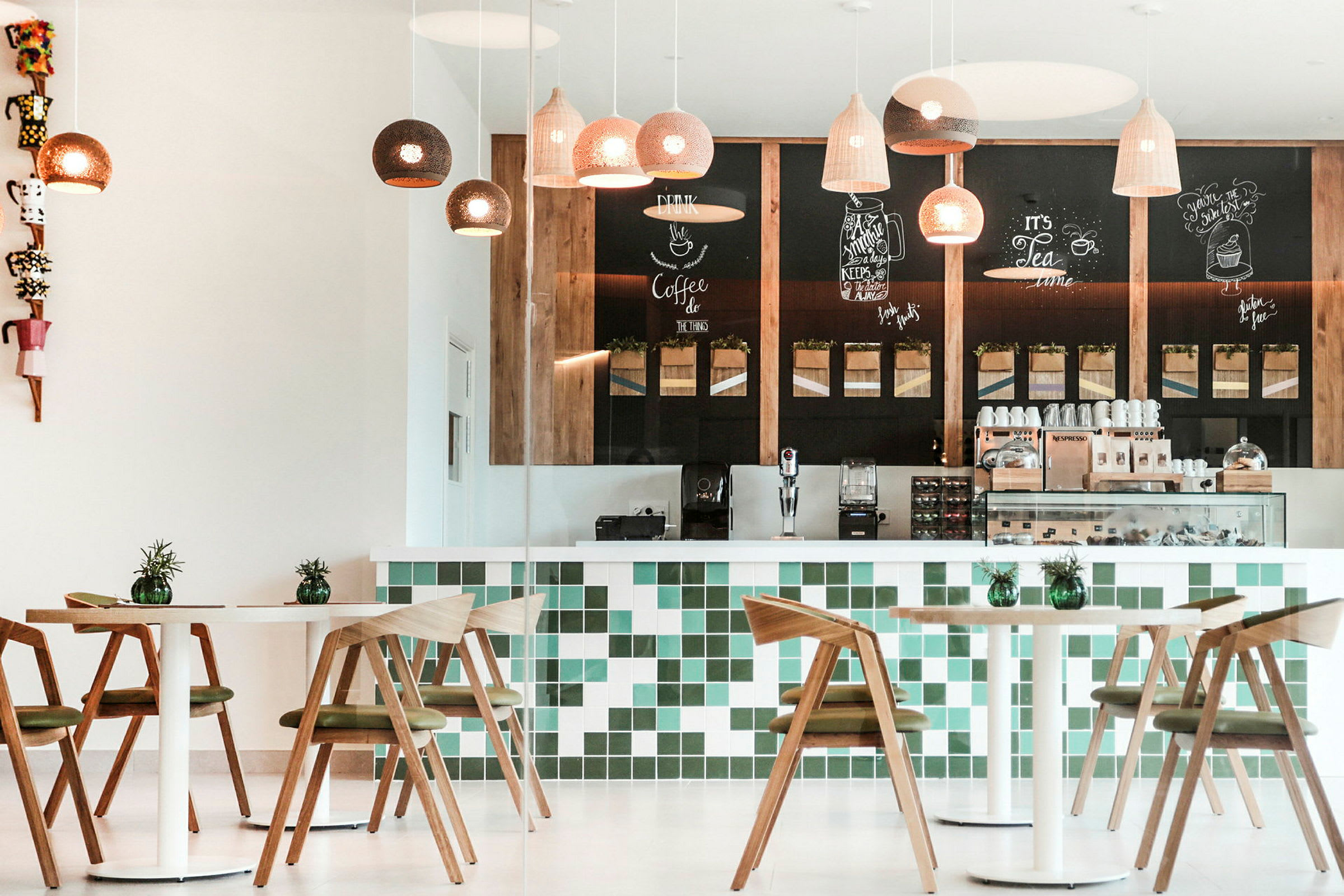 En moderne café med trægulve og hvide borde foran en bardisk dekoreret med grønne og hvide fliser. Loftslamper hænger fra loftet. (AI-genereret tekst)