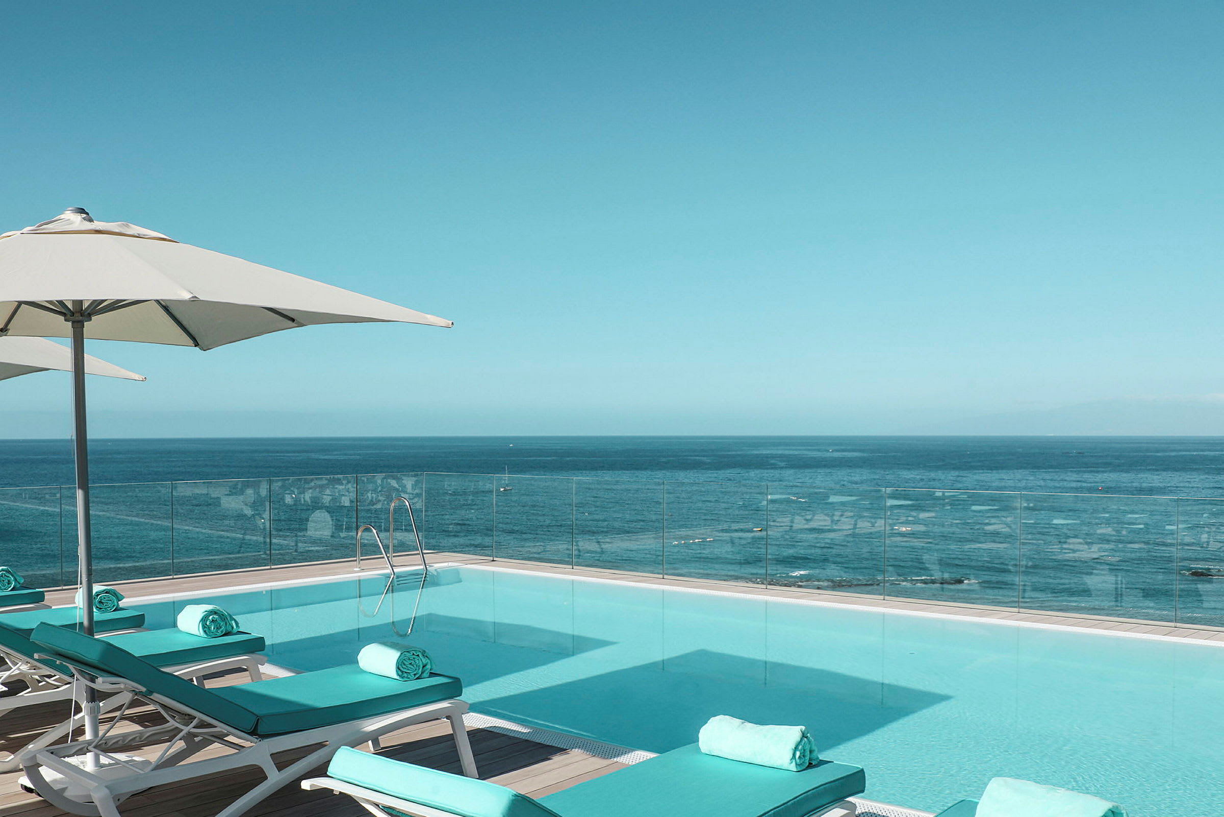 Infinitypool ved havet med liggestole og parasoller. (AI-genereret tekst)