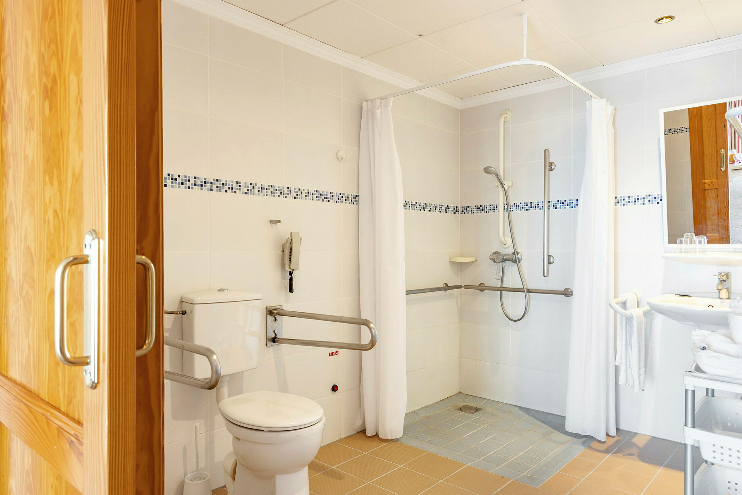 Badeværelse med bruseområde, toilet og håndvask udstyret med støttehåndtag. (AI-genereret tekst)