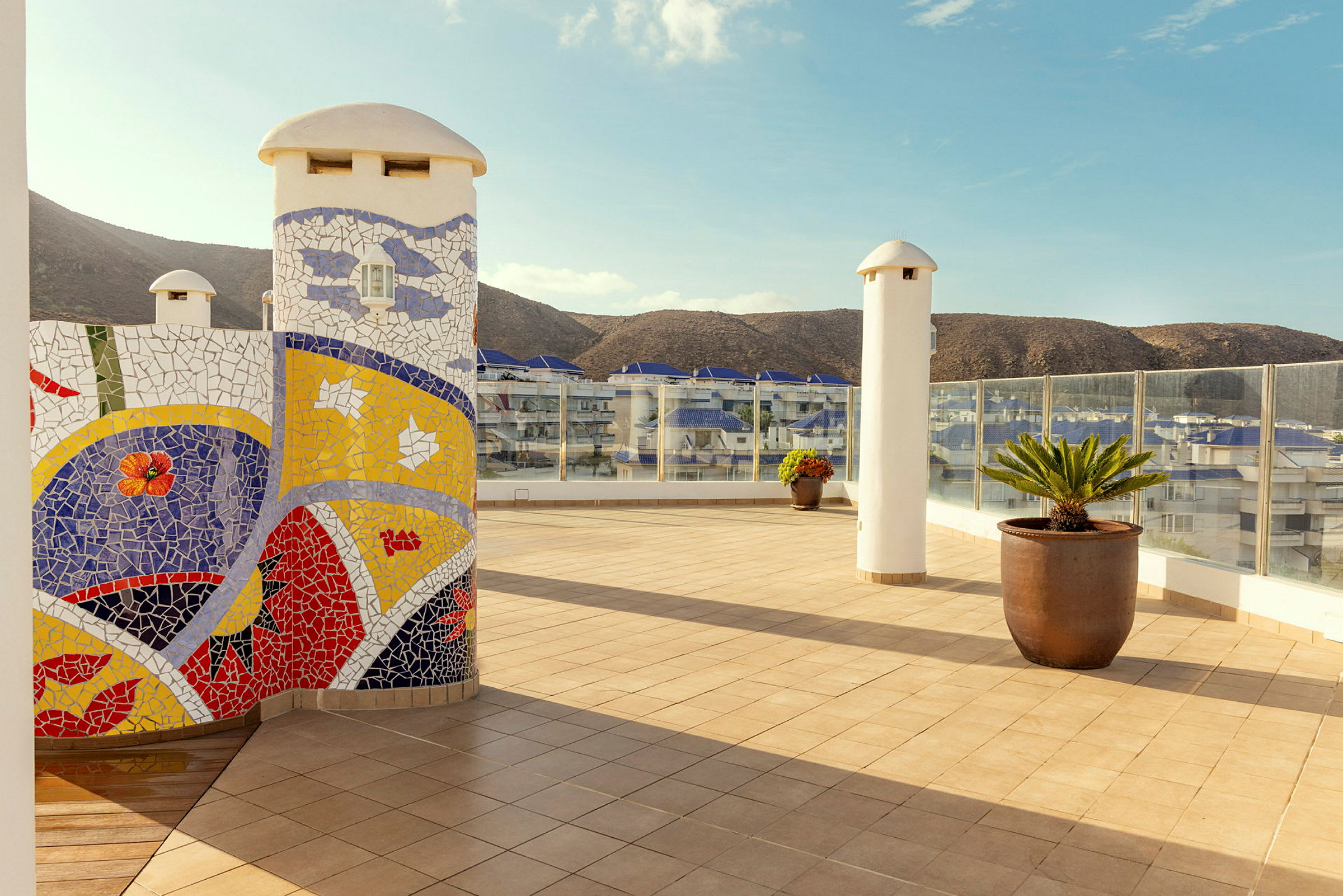 Udendørs terrasse med keramisk mosaik, potteplanter og bjerge i baggrunden. (AI-genereret tekst)