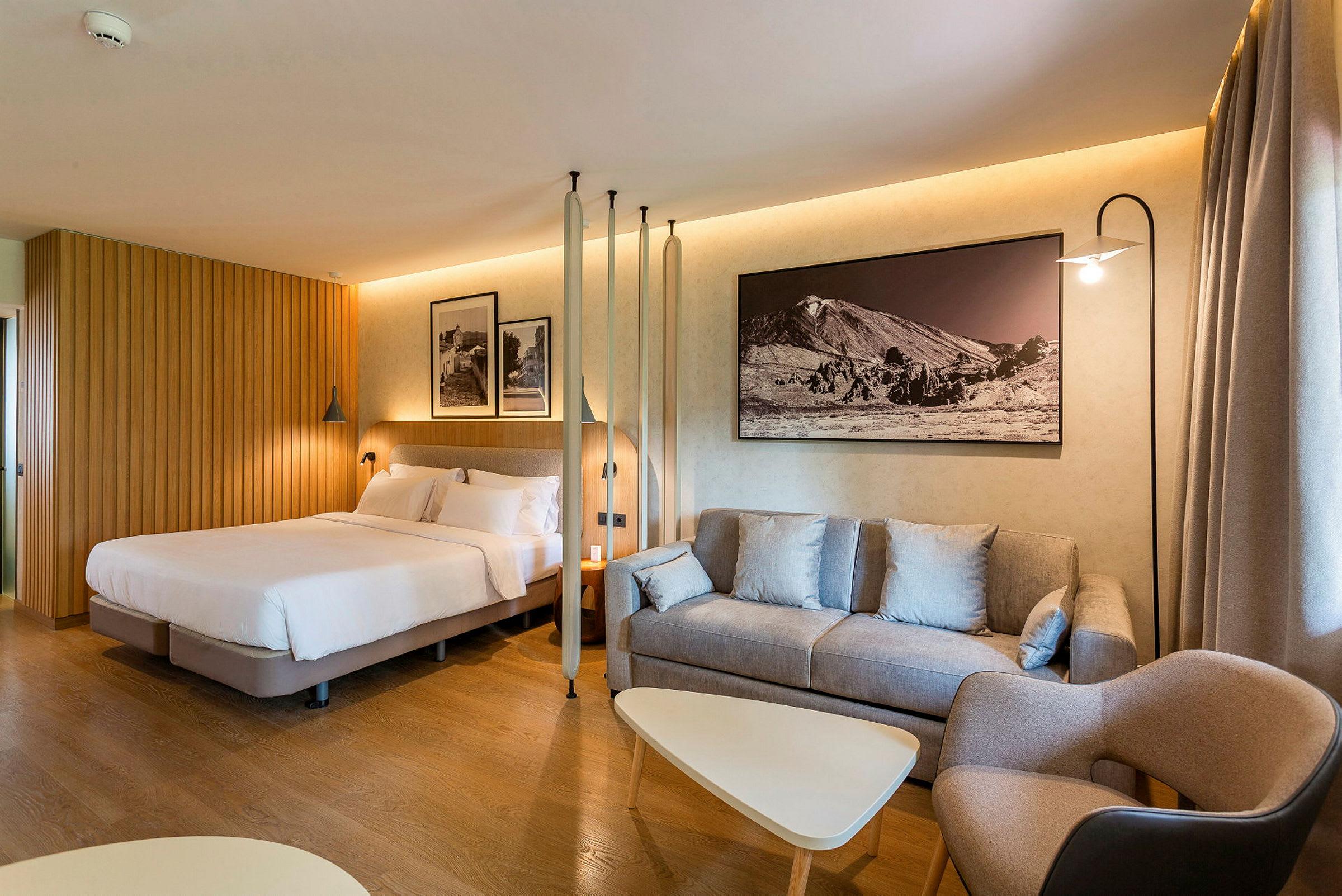 Hotelværelse med seng, sofa og bord samt vægdekoration. (AI-genereret tekst)