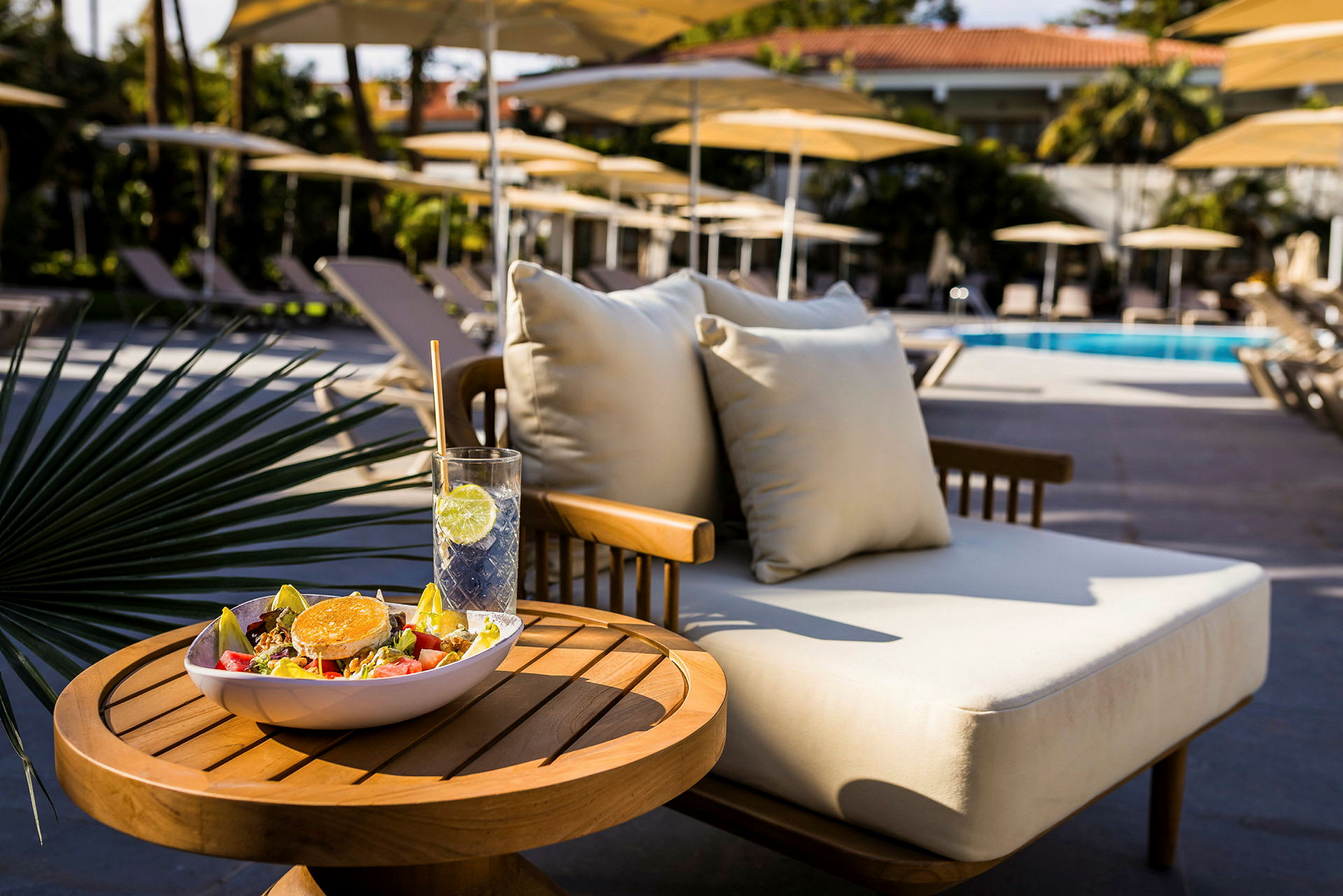 Et bord med en salat og en drink ved siden af en solvogn ved en pool. (AI-genereret tekst)