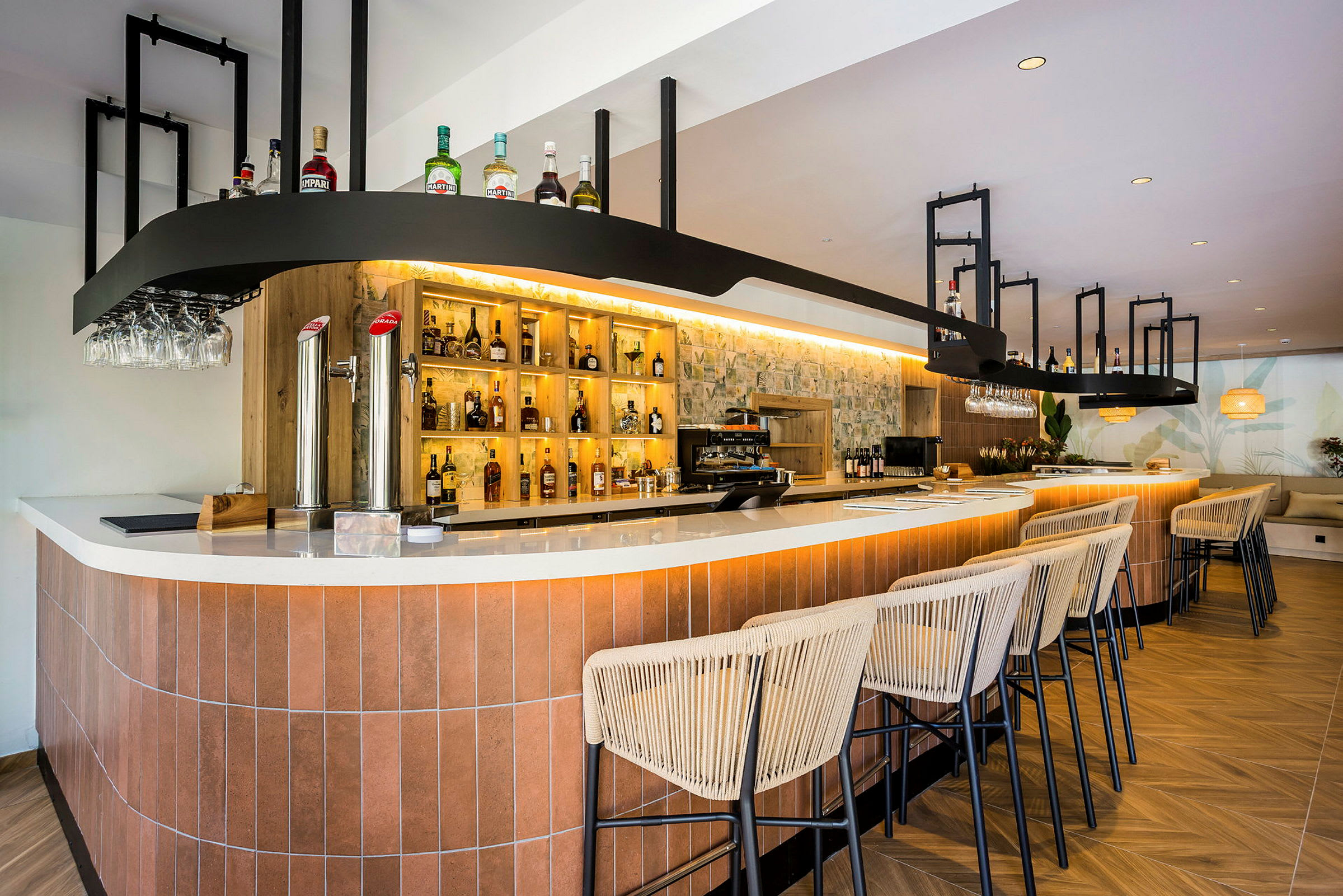 En moderne bar med en lang bardisk, oplyste hylder med flasker og komfortable barstole i træ og stof. (AI-genereret tekst)