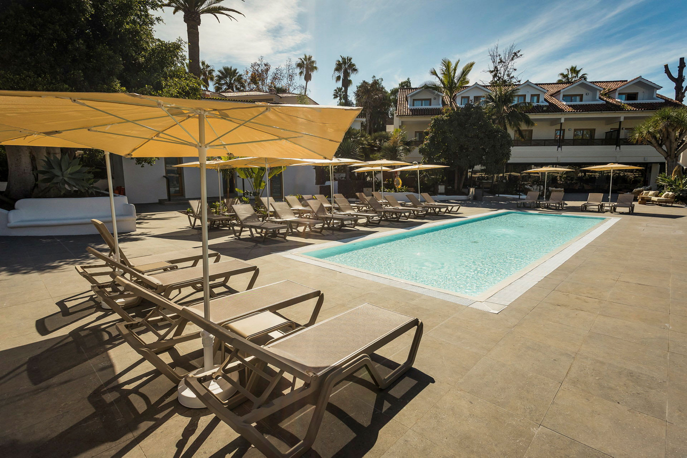 Udendørs pool med liggestole og parasoller i et hotellandskab. (AI-genereret tekst)