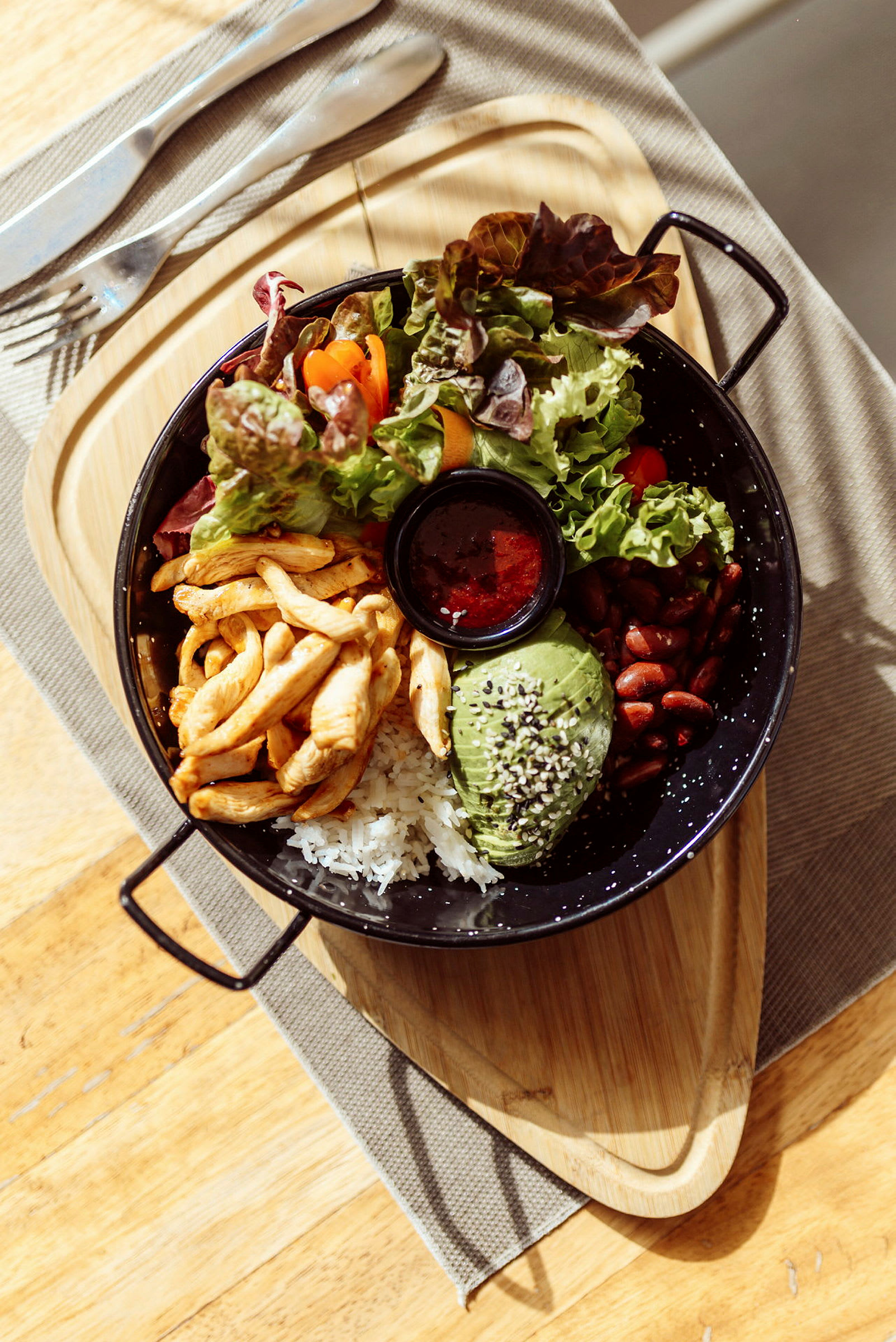 En madportion med kylling, ris, avocado, bønner, salat og sauce. (AI-genereret tekst)