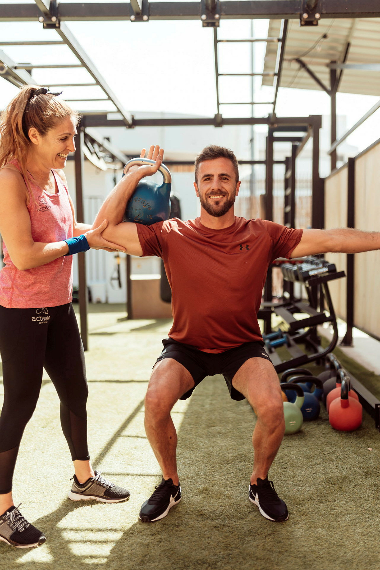 Person træner med kettlebell og får hjælp udendørs. (AI-genereret tekst)
