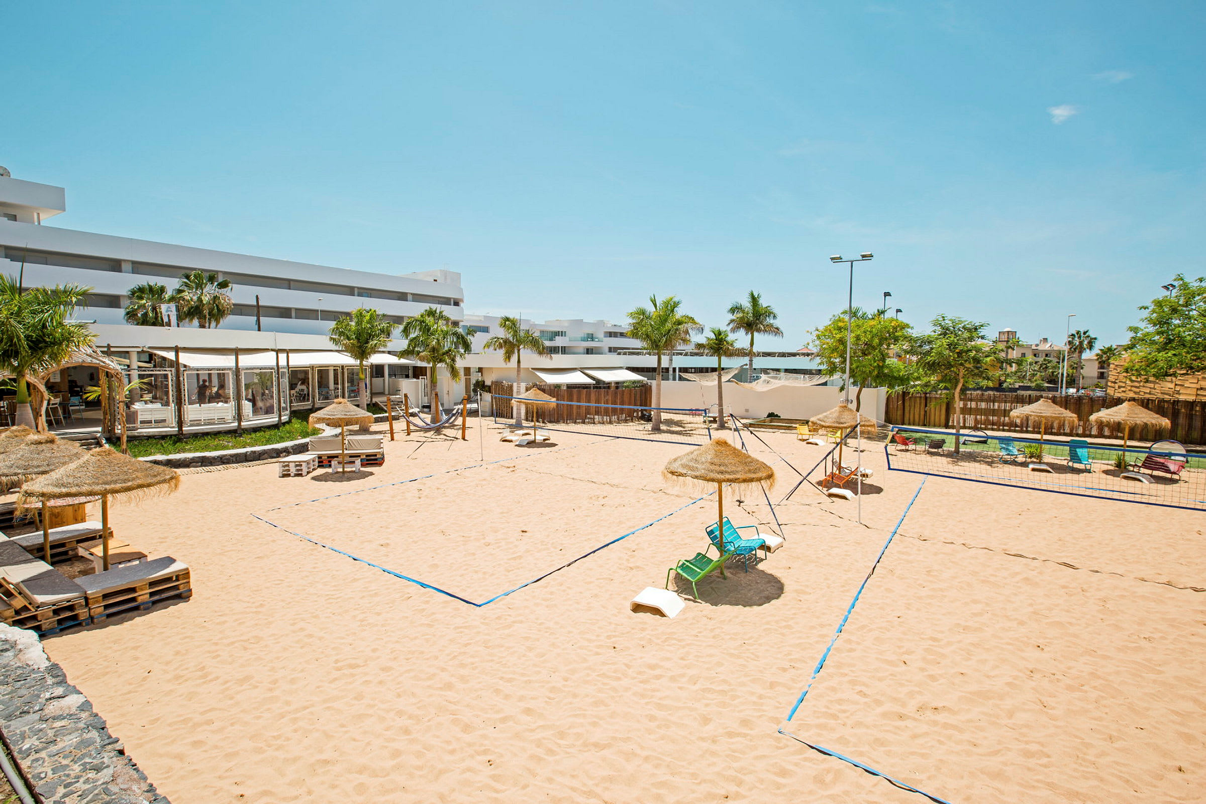 Billede af en sandvolleyballbane med parasoller og liggestole omkring. (AI-genereret tekst)