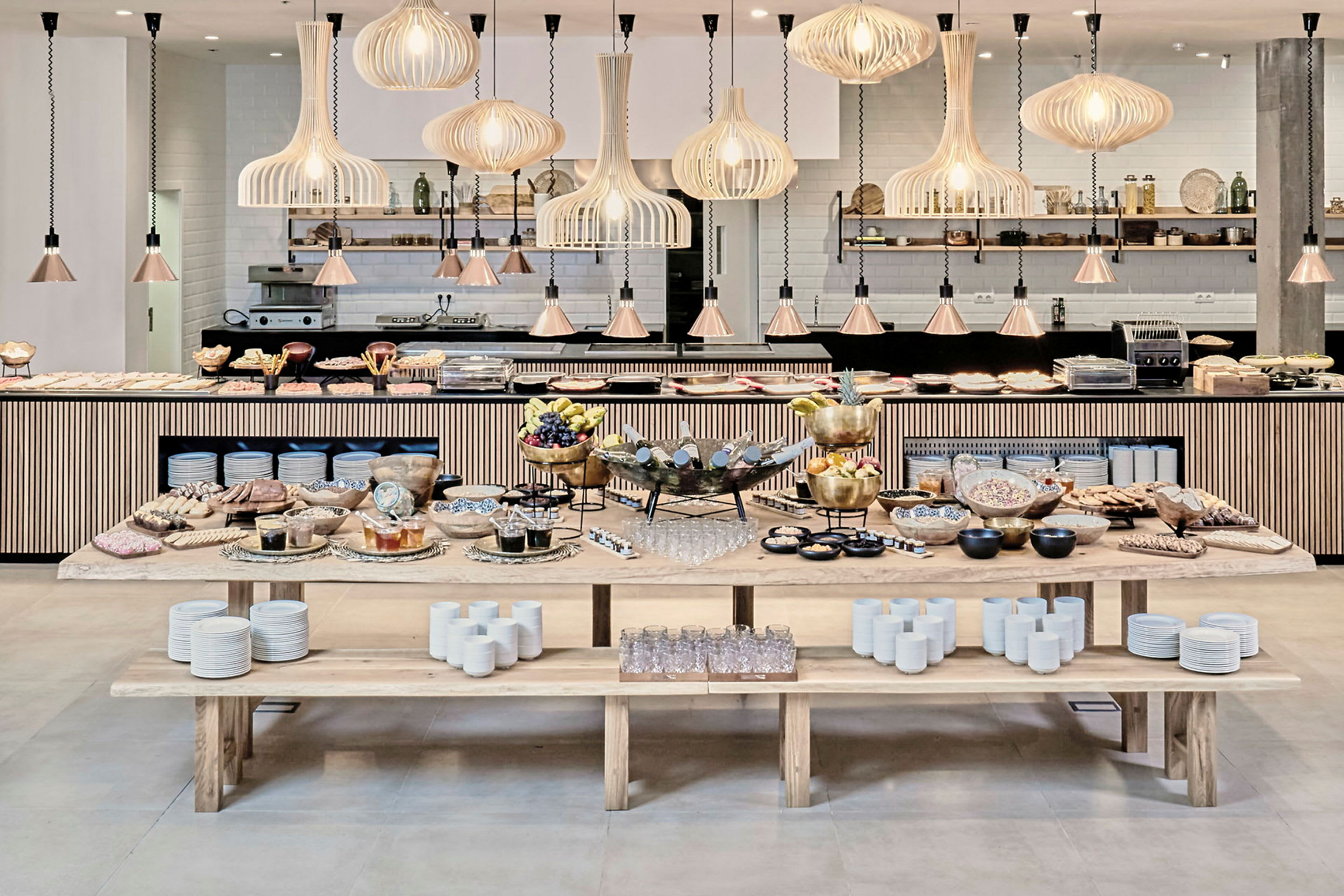 En buffet med forskellige retter og frugter samt glas og porcelæn på træborde i en stilfuldt indrettet restaurant. (AI-genereret tekst)