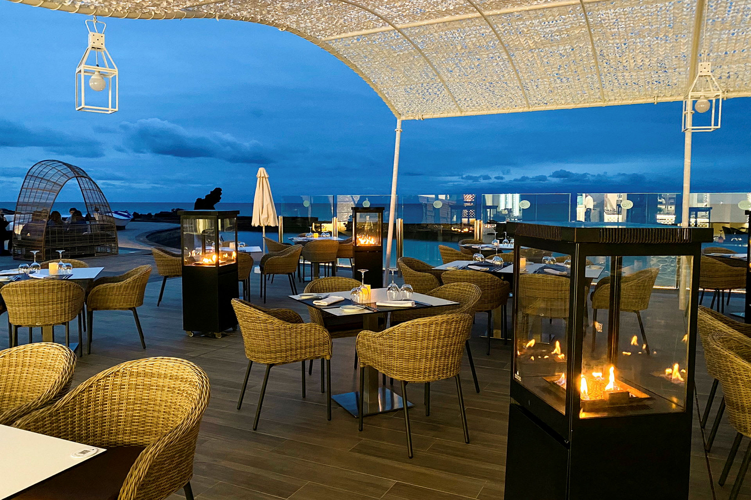 Udendørsrestaurant med borde, stole og pejse under aftenshimlen. (AI-genereret tekst)