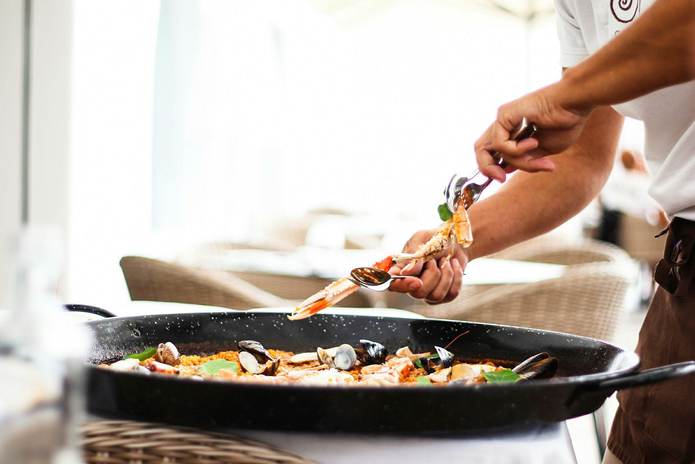 En person lægger mad fra en paellapande med et serveringsredskab. (AI-genereret tekst)