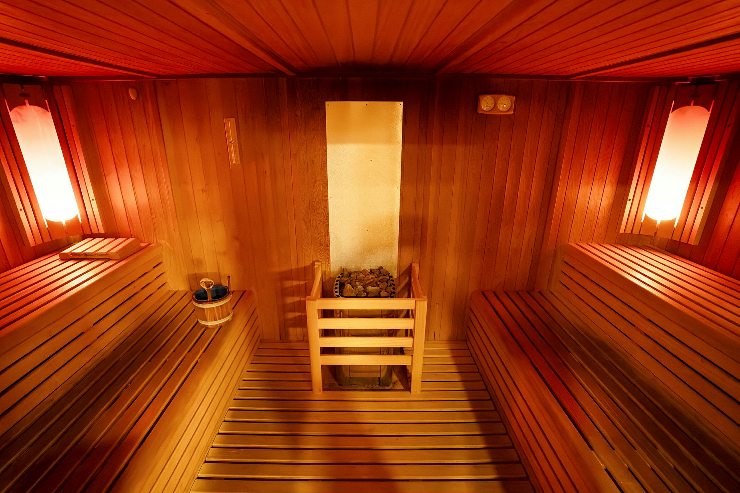 En indvendig af en sauna med træpaneler, siddepladser på begge sider og en varmekilde i midten. (AI-genereret tekst)