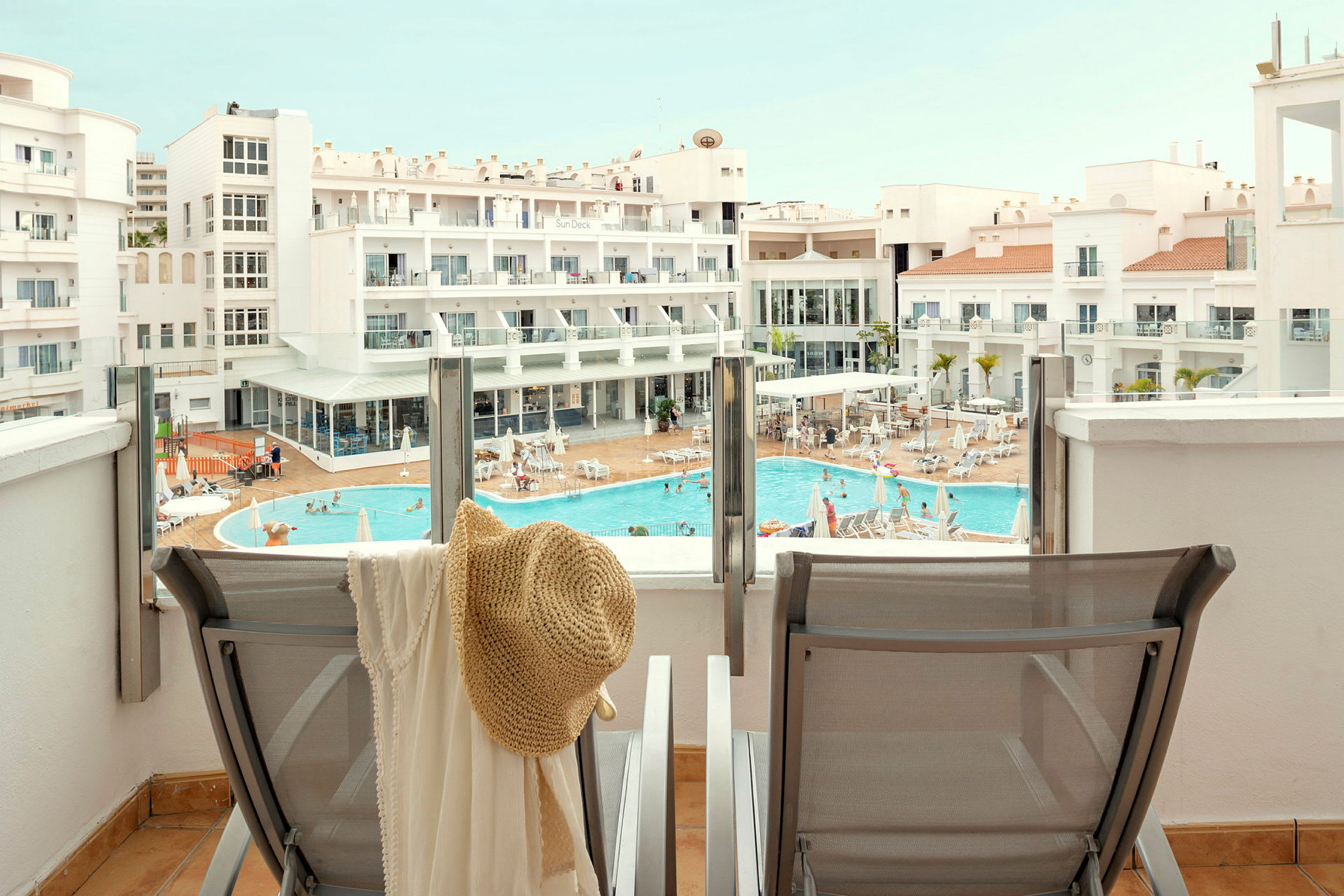 Udsigt fra en terrasse over en pool og hotelbygning. (AI-genereret tekst)