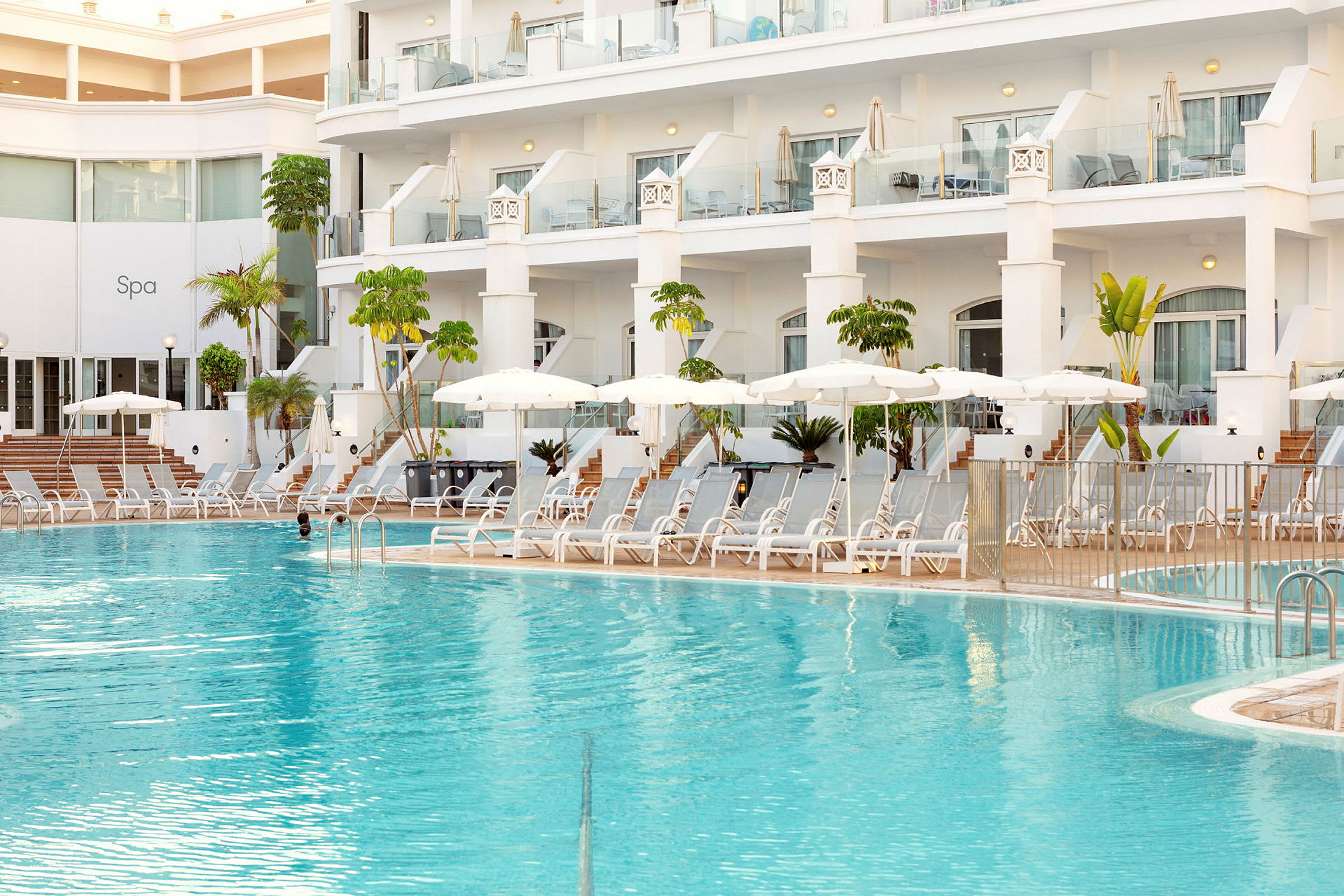 Hotelpool med liggestole og parasoller ved en moderne bygning. (AI-genereret tekst)