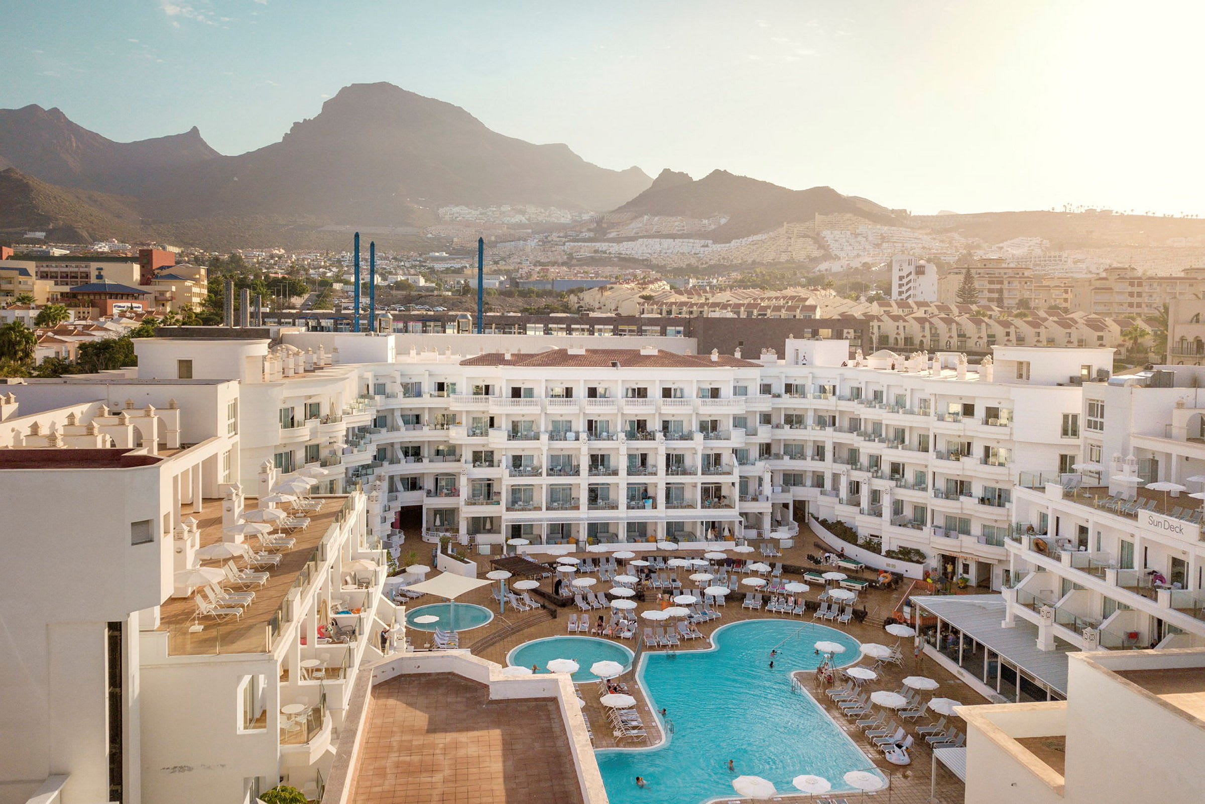 Udsigt over hotelområdet med pools og omkringliggende bjerge. (AI-genereret tekst)