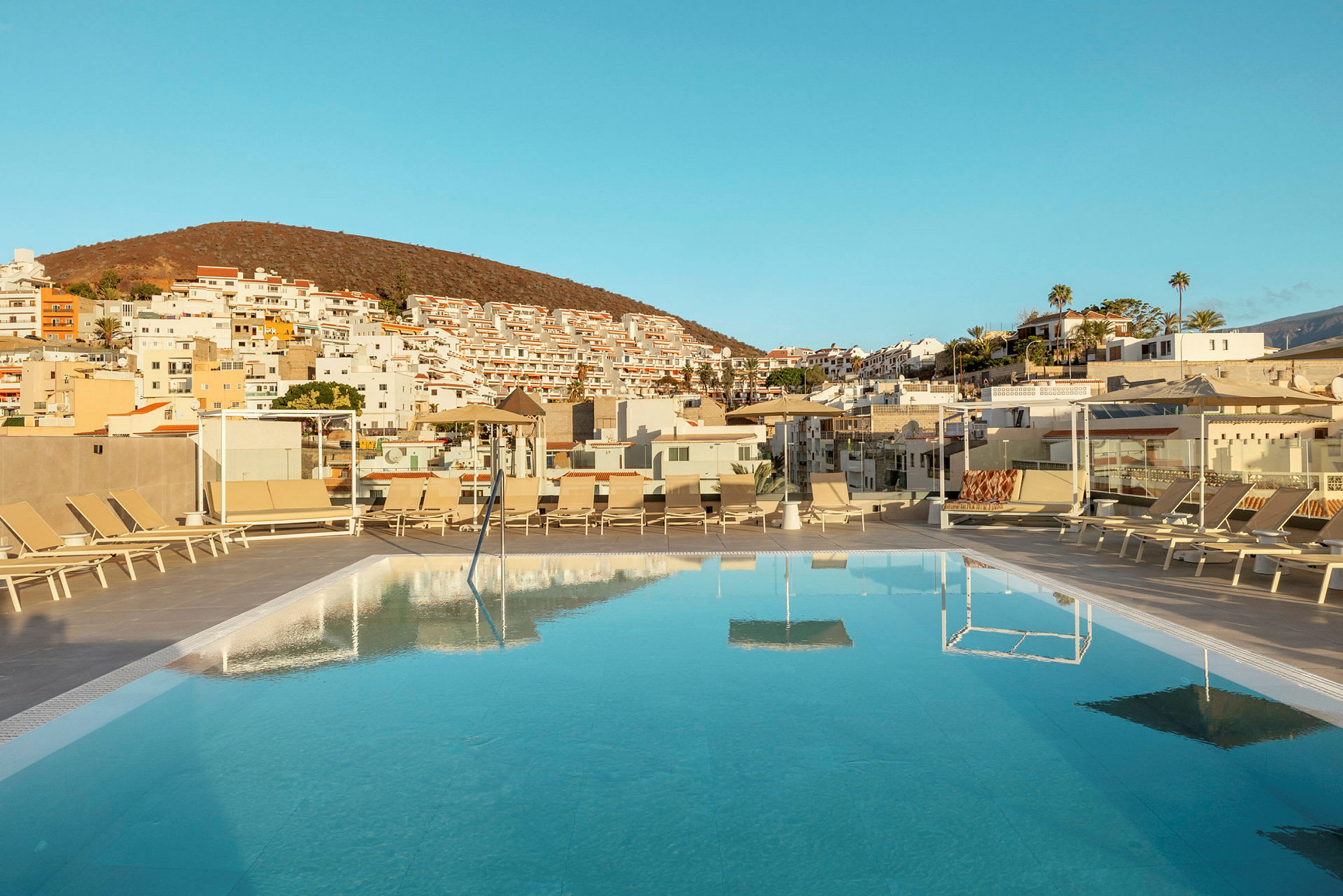 En swimmingpool med liggestole på en terrasse og huse i baggrunden. (AI-genereret tekst)