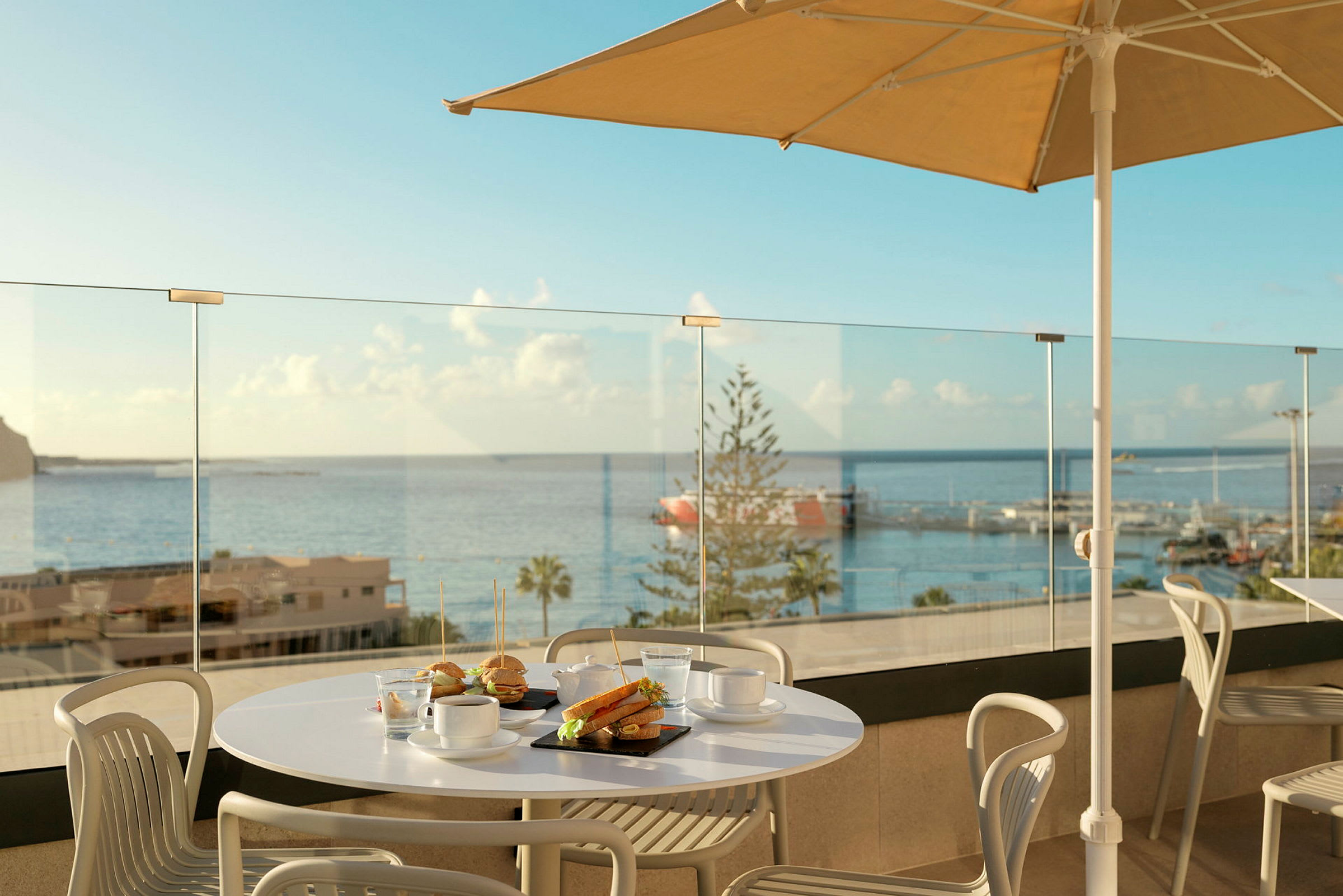 En spiseplads med bord og stole på en terrasse med udsigt over havet. (AI-genereret tekst)