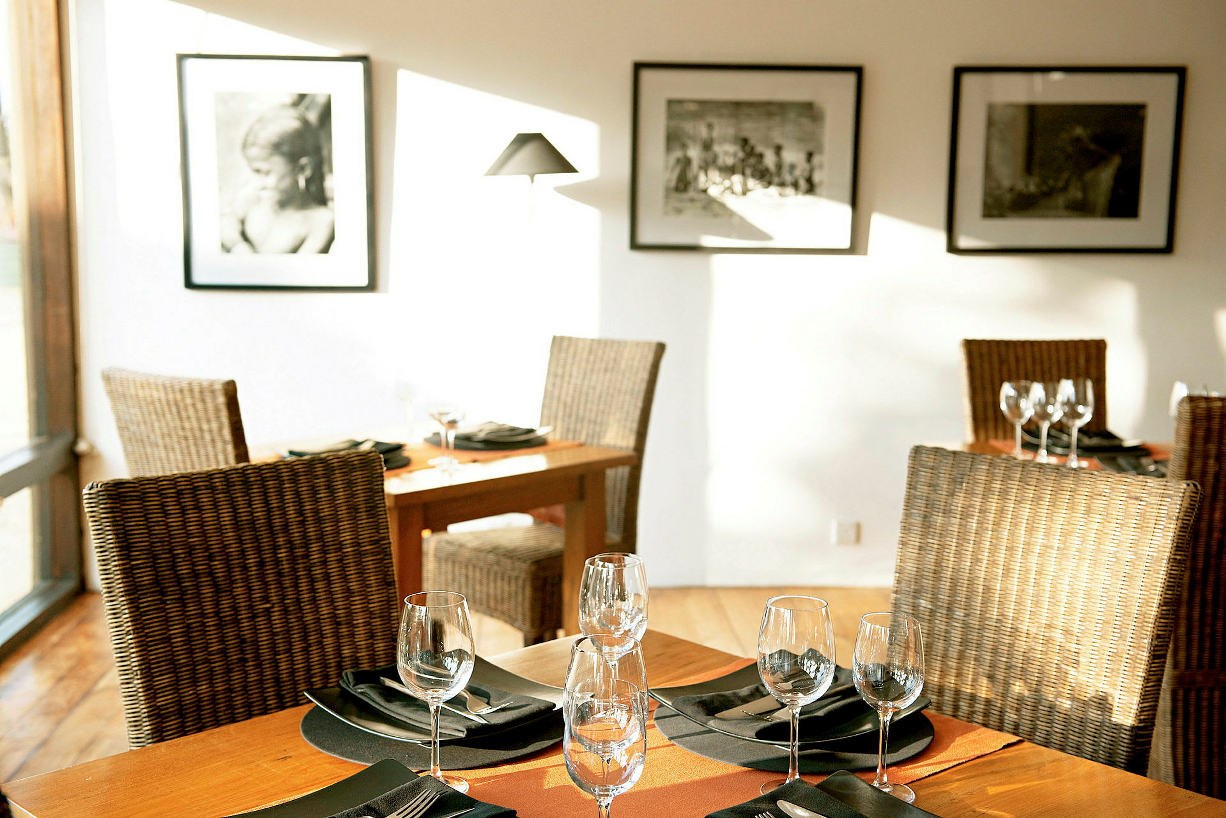 Et elegant restaurantbord med opdækning, omgivet af rottingstole og dekoreret med glas og servietter. Væggene er pyntet med sort-hvide fotografier. (AI-genereret tekst)