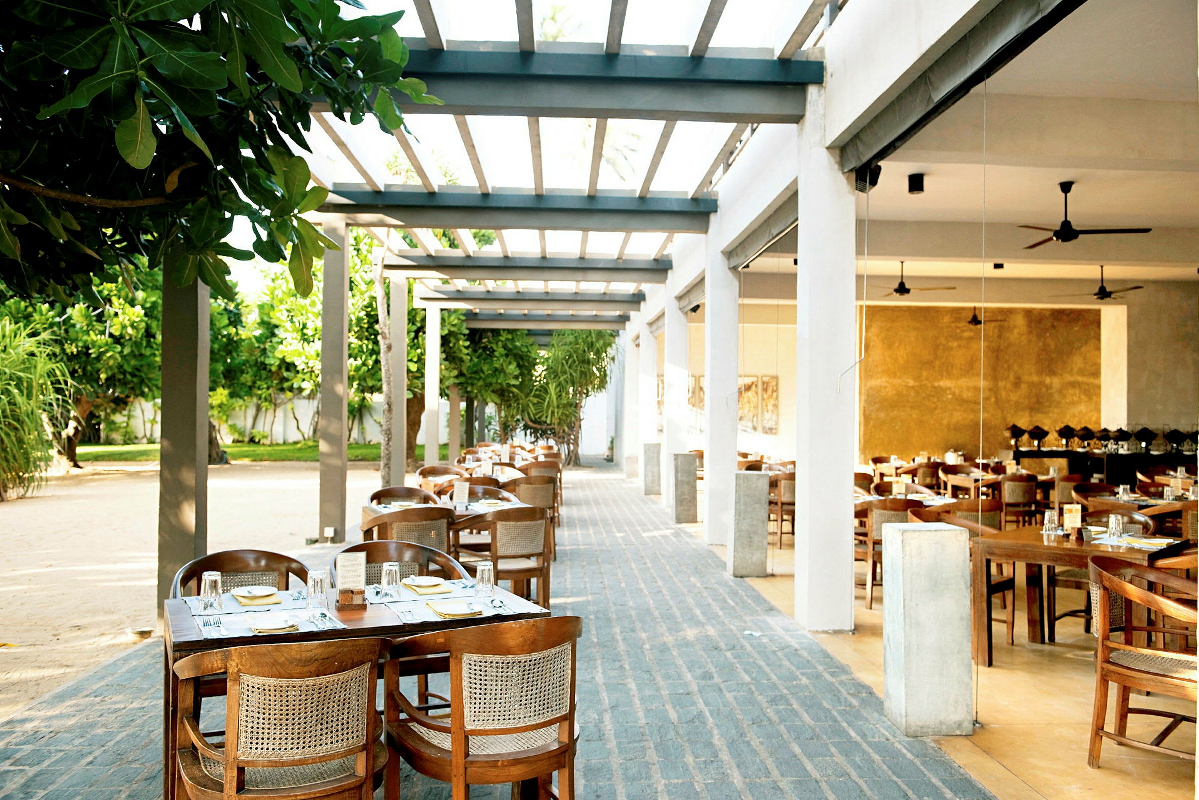 Udendørs restaurant med borde og stole arrangeret under en pergola. (AI-genereret tekst)