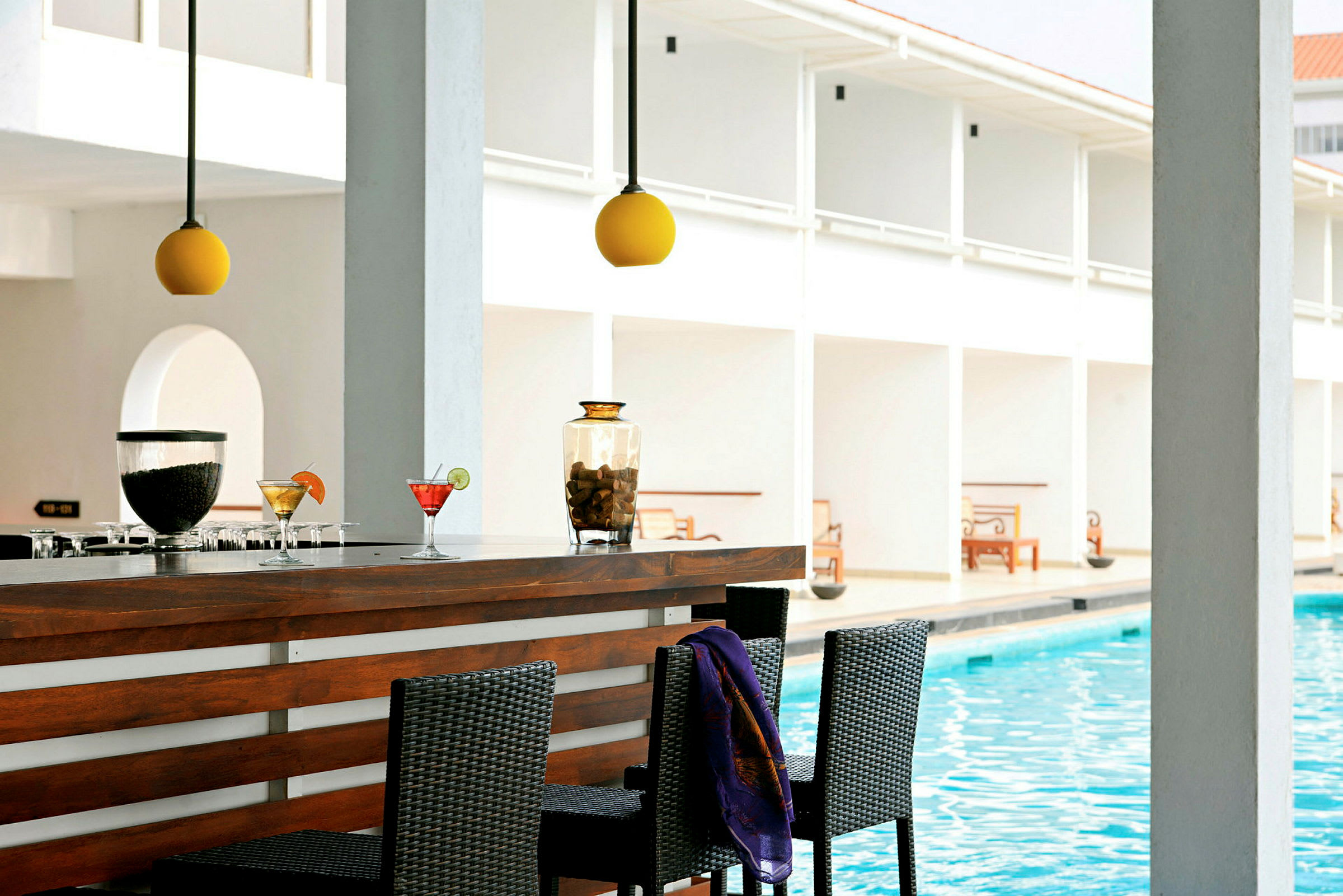 En bar ved en pool med nogle drinks samt belysning ovenover og siddepladser foran. (AI-genereret tekst)