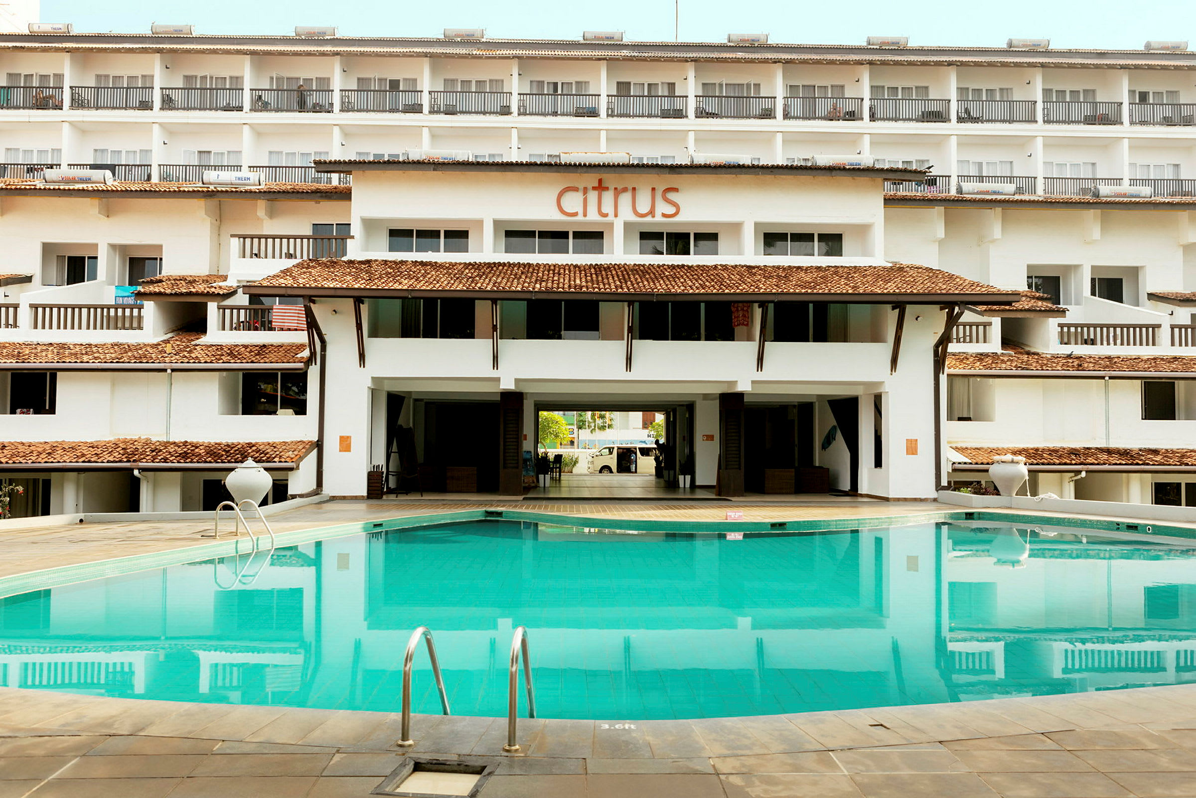 En pool foran en bygning med flere lejligheder og et skilt med teksten "Citrus" på facaden. (AI-genereret tekst)