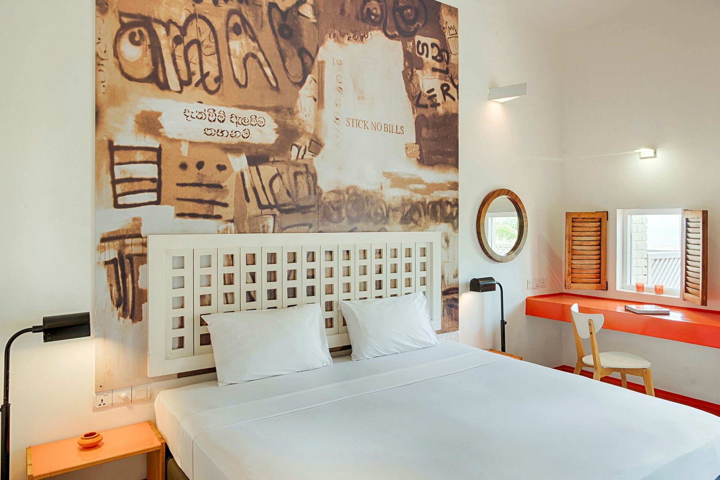 Et hotelværelse med en dobbeltseng, et billede med graffiti-lignende kunst på væggen bag sengen og et skrivebord med spejl og stol. (AI-genereret tekst)