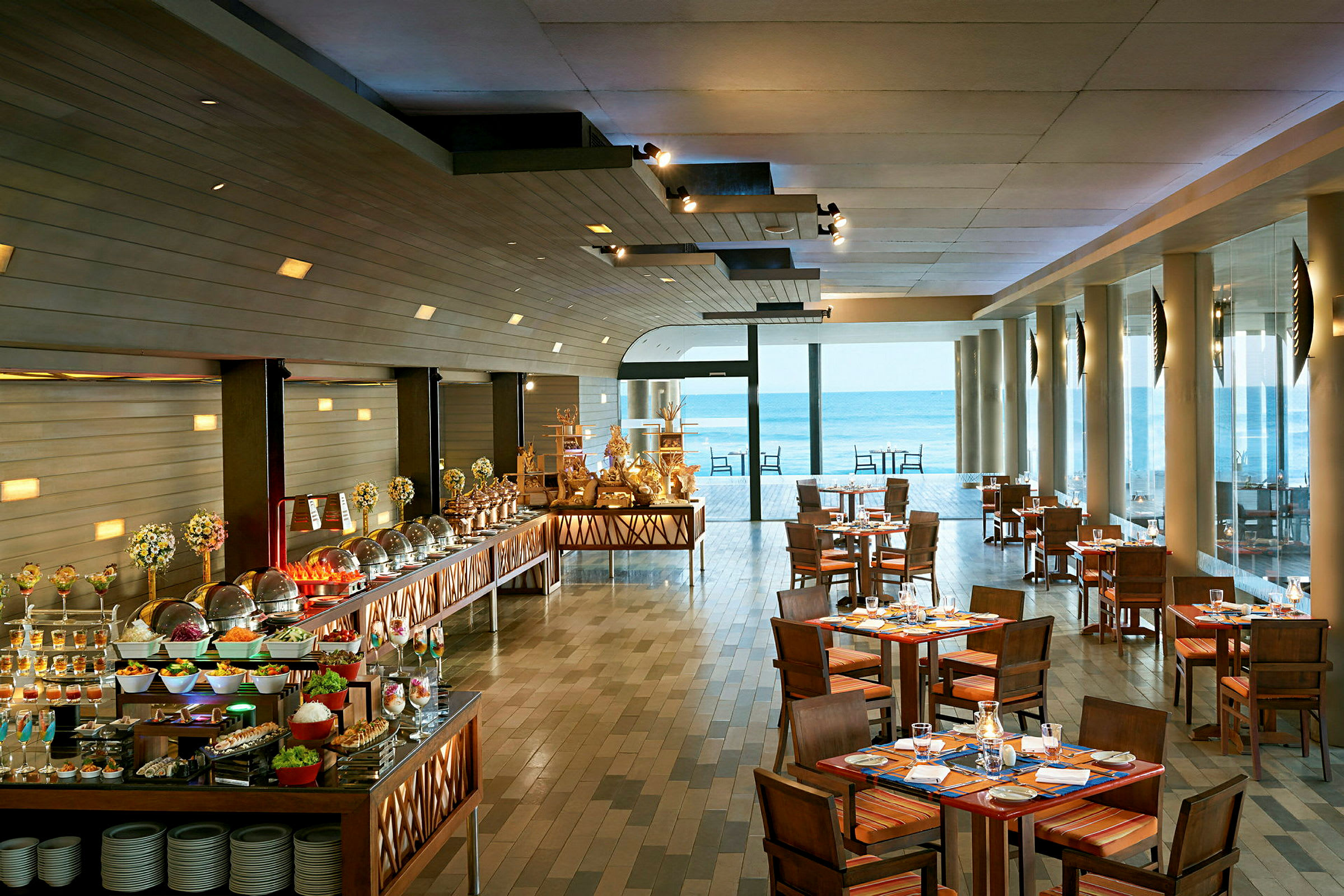 Billede af en restaurant med opdækkede borde og en buffet med forskellige retter samt store vinduer med udsigt til havet. (AI-genereret tekst)