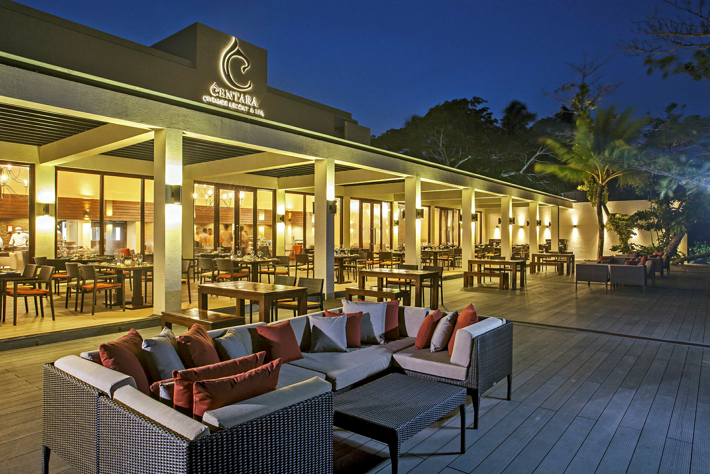 En udendørs terrasse ved en restaurant med borde, stole og sofagrupper i skumringslys. (AI-genereret tekst)