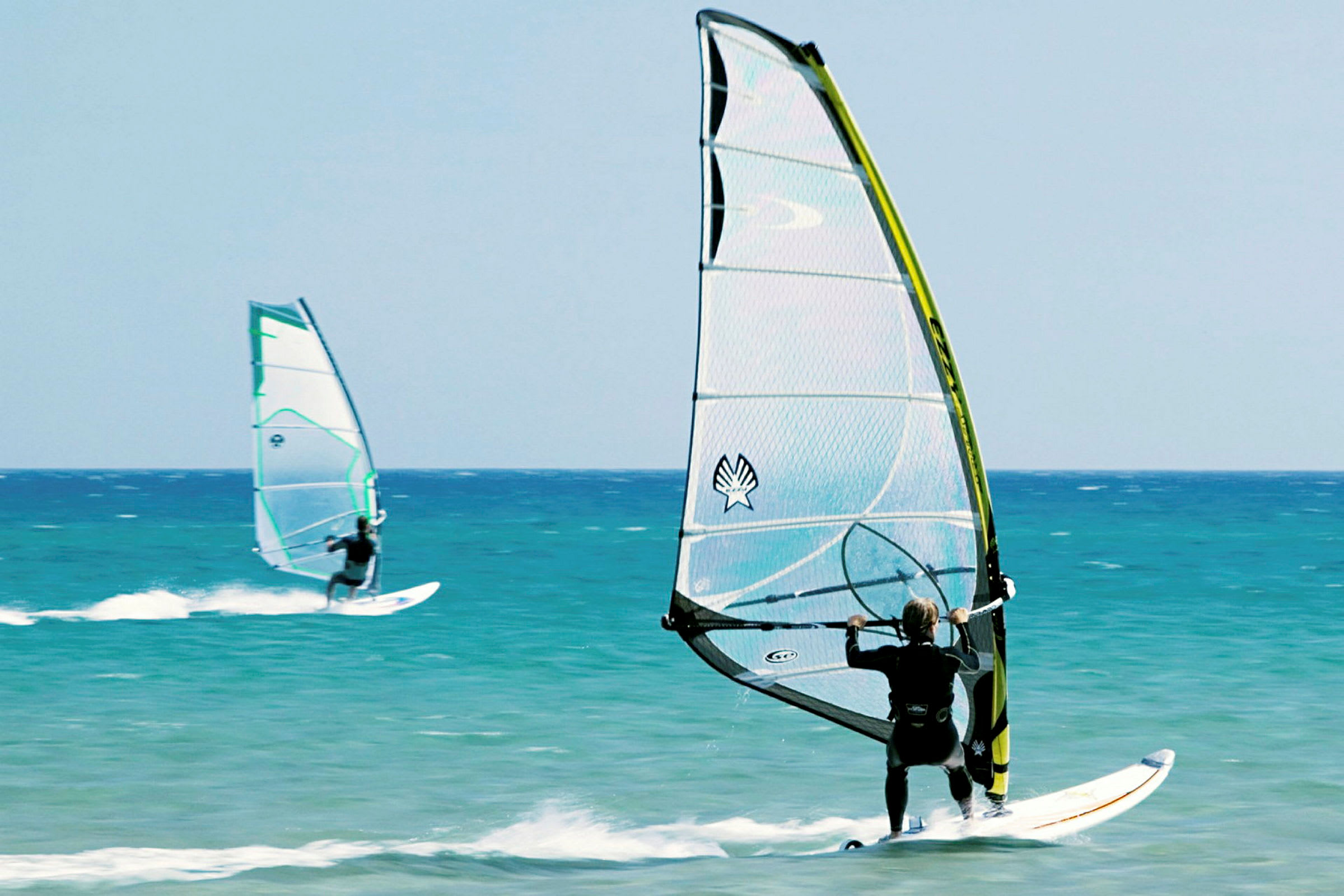 To personer windsurfer på havet under en klar himmel. (AI-genereret tekst)