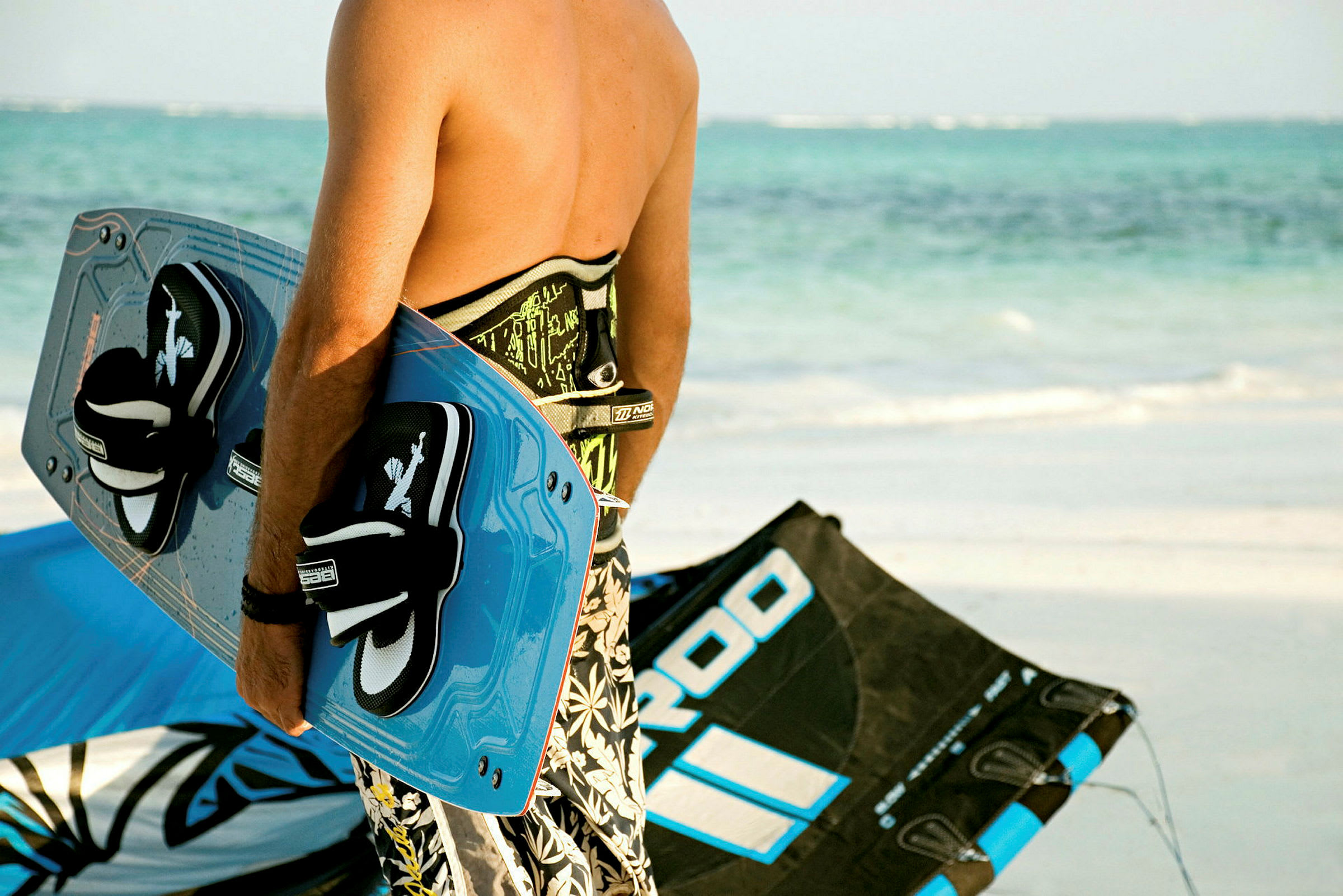 En person holder et kiteboard og står tæt på en kite på en sandstrand. (AI-genereret tekst)